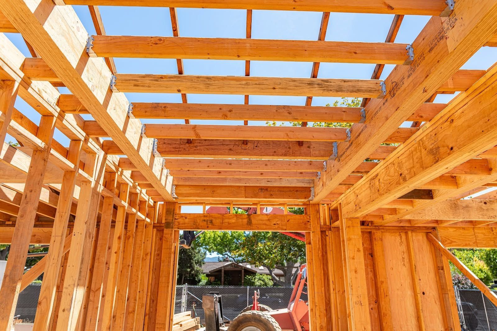 Interior of a wooden house under construction, with exposed framing and roof beams visible through open walls.