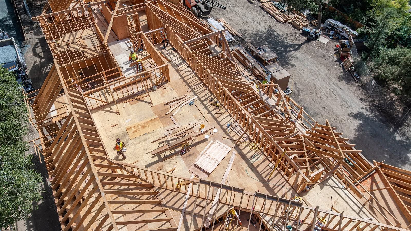 Aerial view of a wooden house frame under construction, with roof trusses and exposed beams.