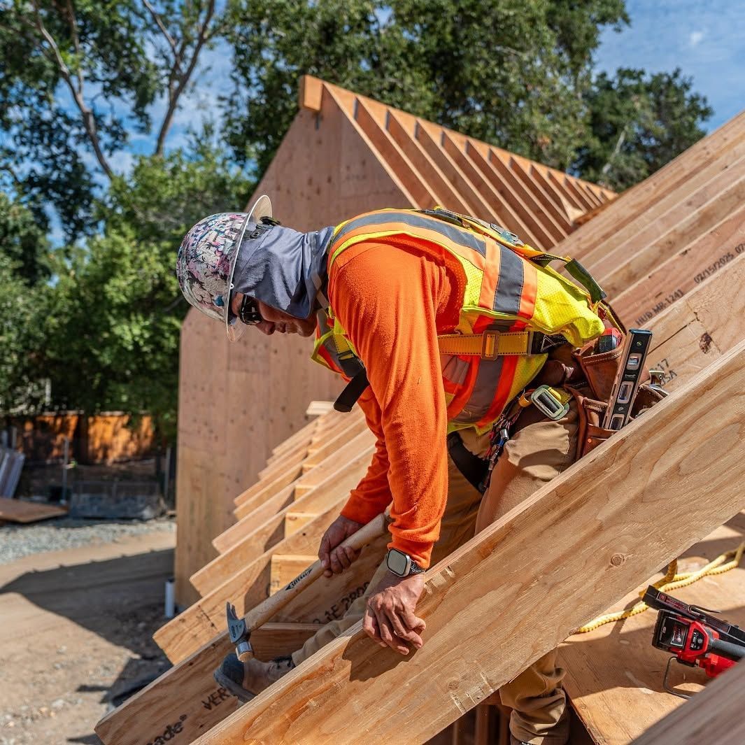 Construction worker in orange safety gear installing wooden roof framing on a house