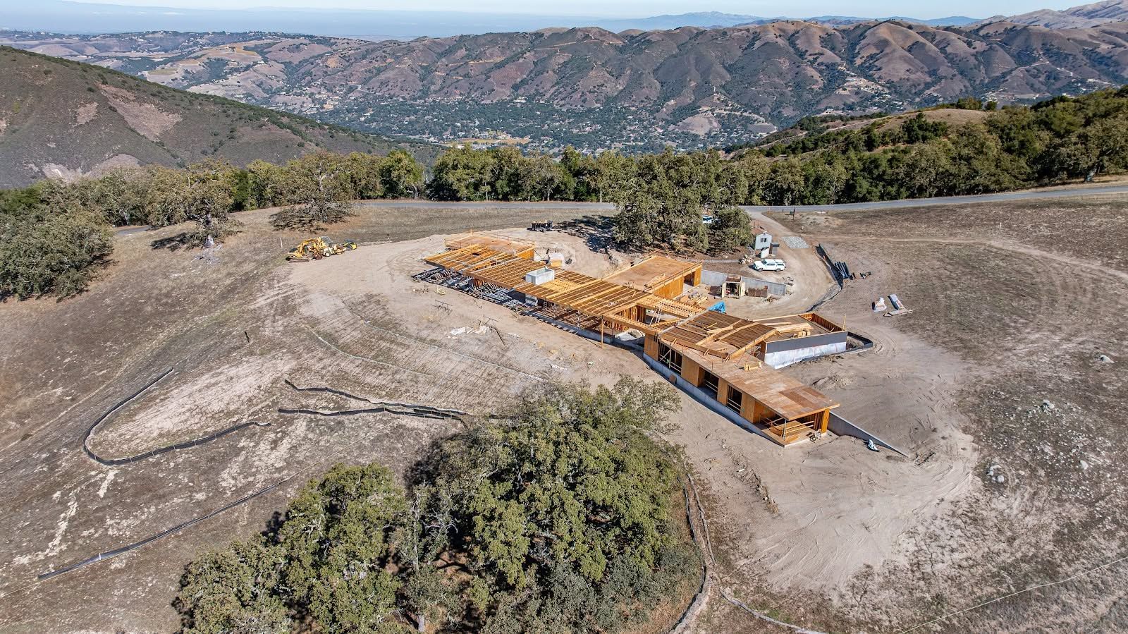Aerial view of a mountain construction site with orange machinery and a wooden platform amid rocky terrain.