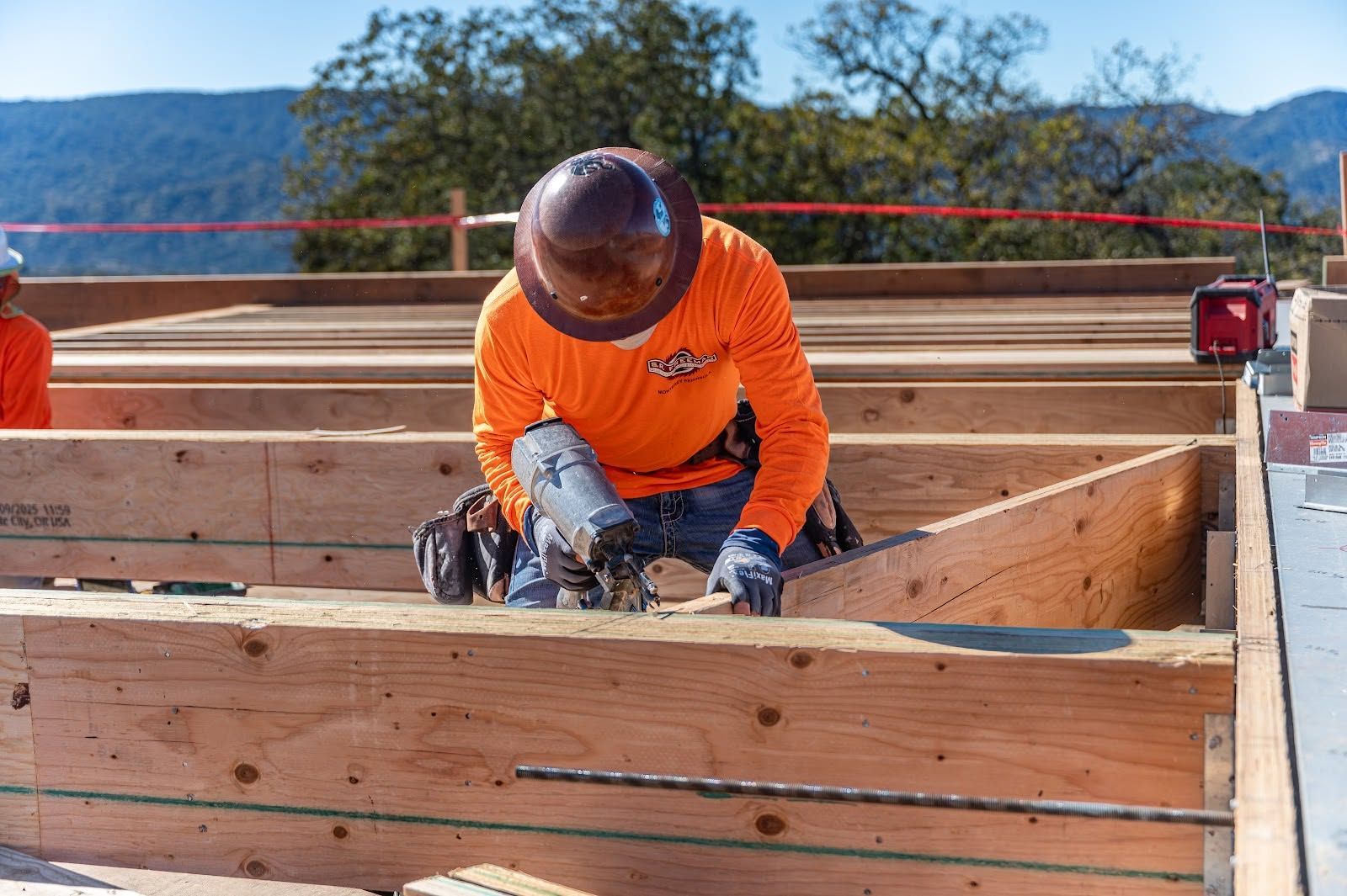 Construction worker in orange safety gear nailing wooden formwork on a job site