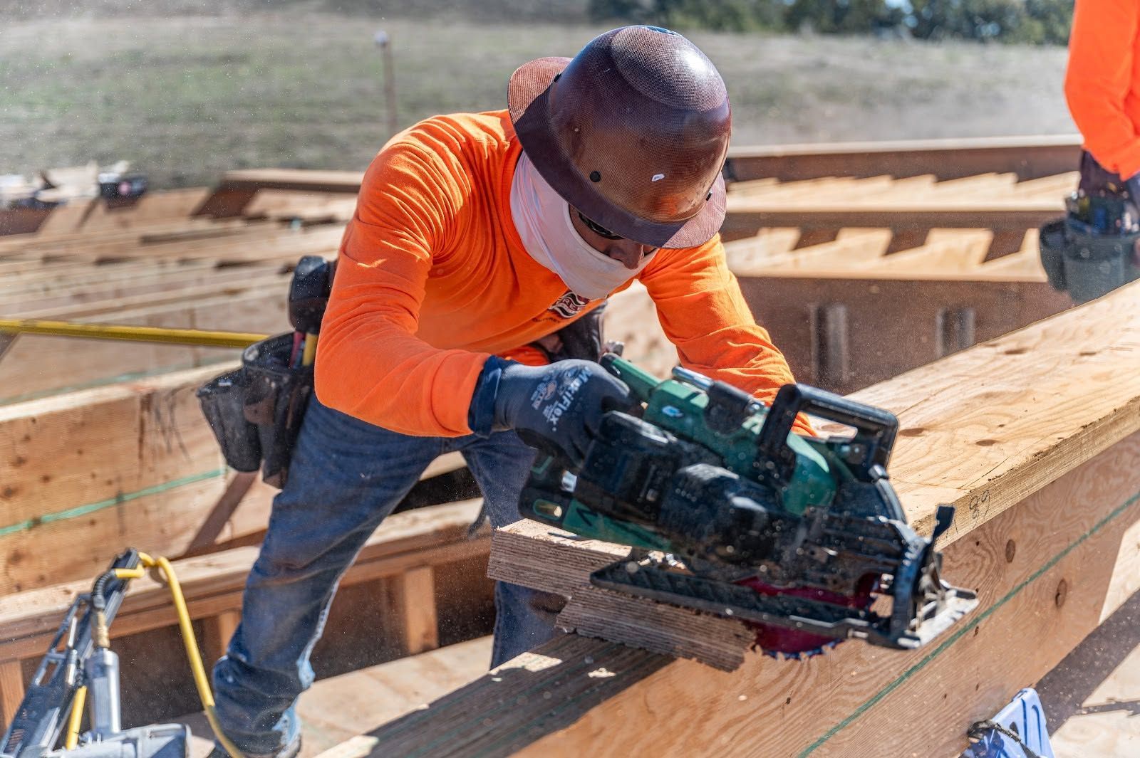 Worker in orange shirt using a circular saw to cut wood on a construction site