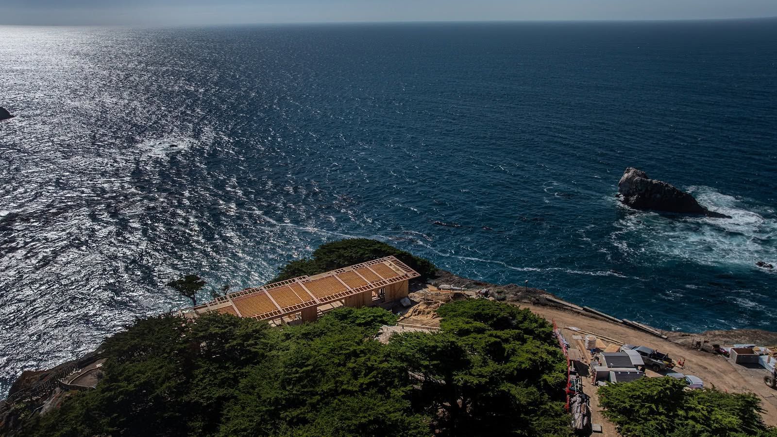 Cliffside coastal overlook with turquoise ocean, rocky shore, and a small pavilion in bright sunlight