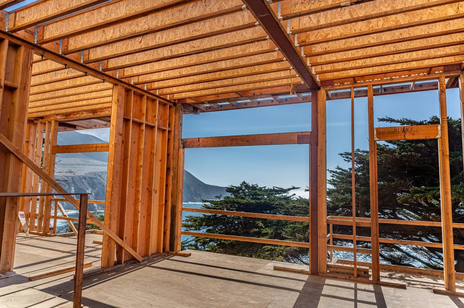Wooden room under construction with open windows overlooking a coastal view