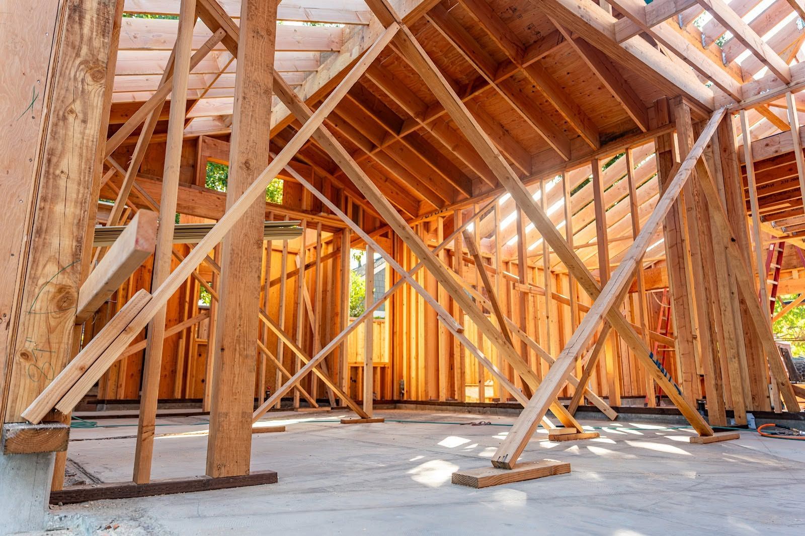 Wooden house framing under construction with exposed beams and roof trusses on a concrete slab