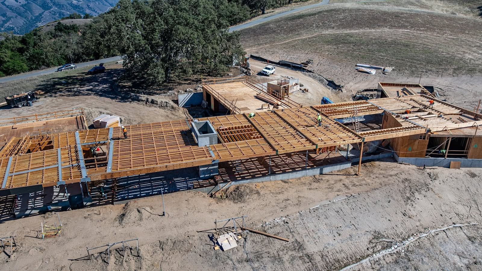 Aerial view of a large wooden house frame under construction on a dry hillside site