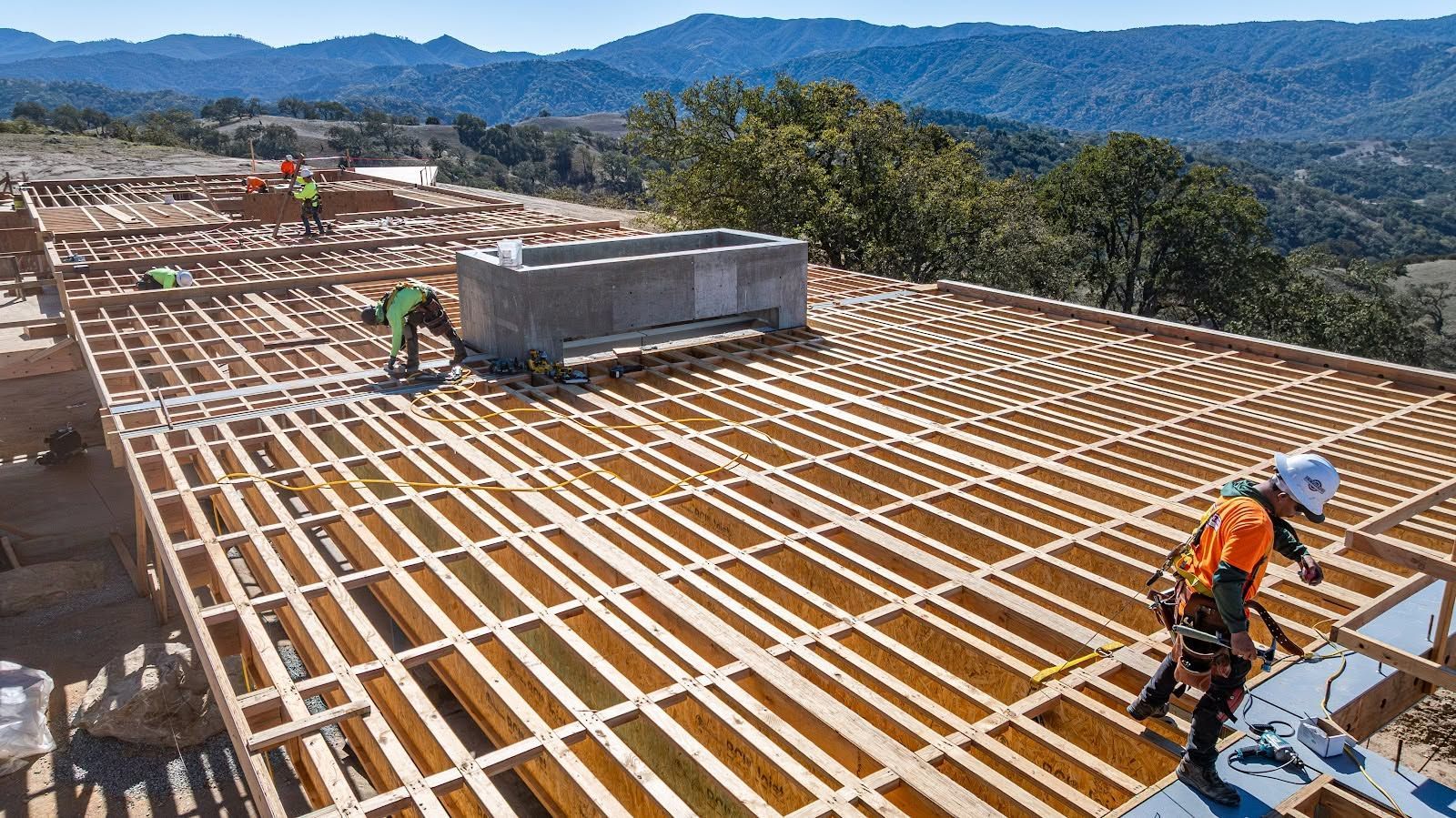 Workers installing rooftop solar panels on a large roof with mountains in the background