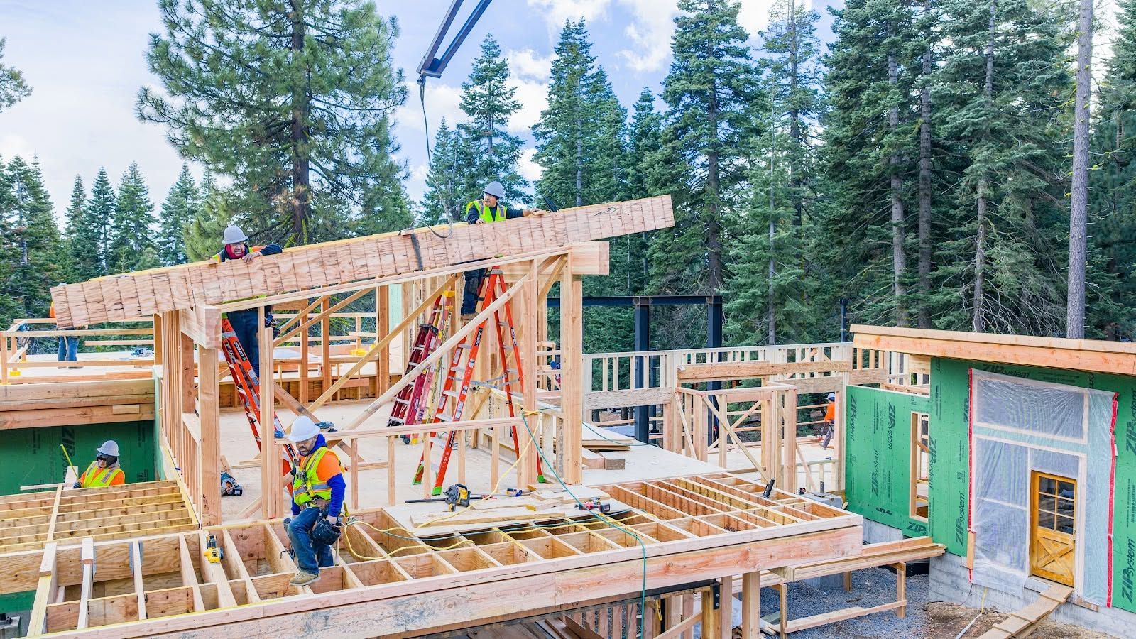Construction site with wooden frame houses and workers amid tall pine trees