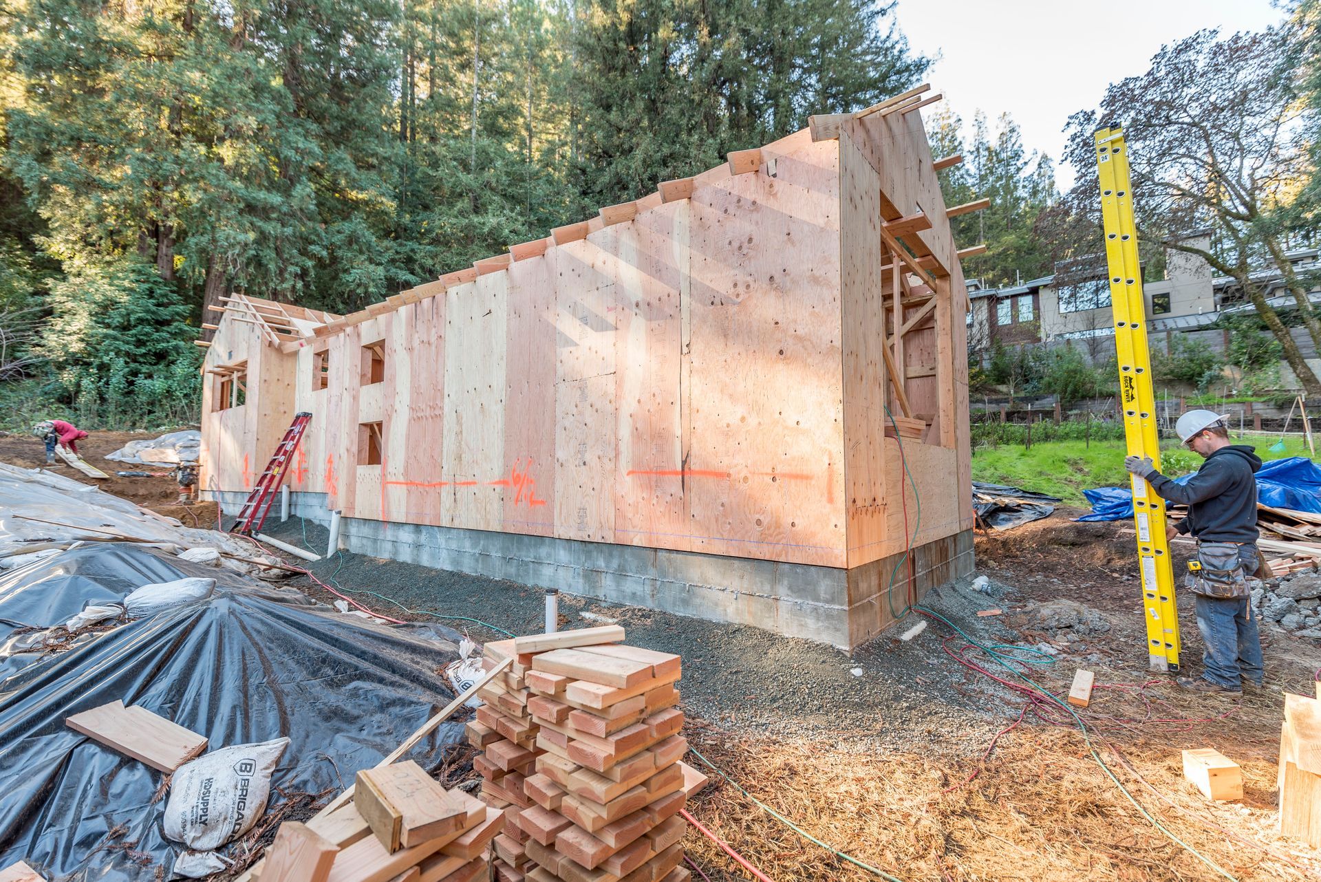 House under construction with plywood sheathing, debris, and forested surroundings