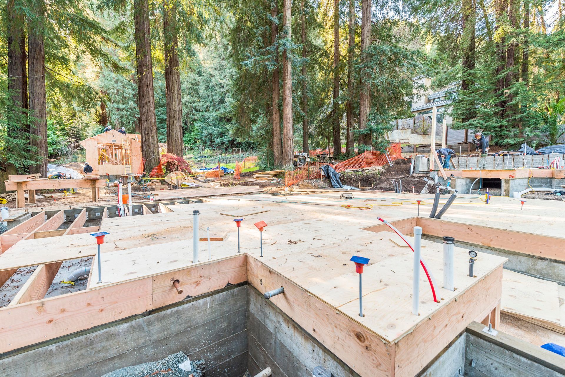 Construction site with concrete foundation forms and scattered tools among tall trees in a wooded area