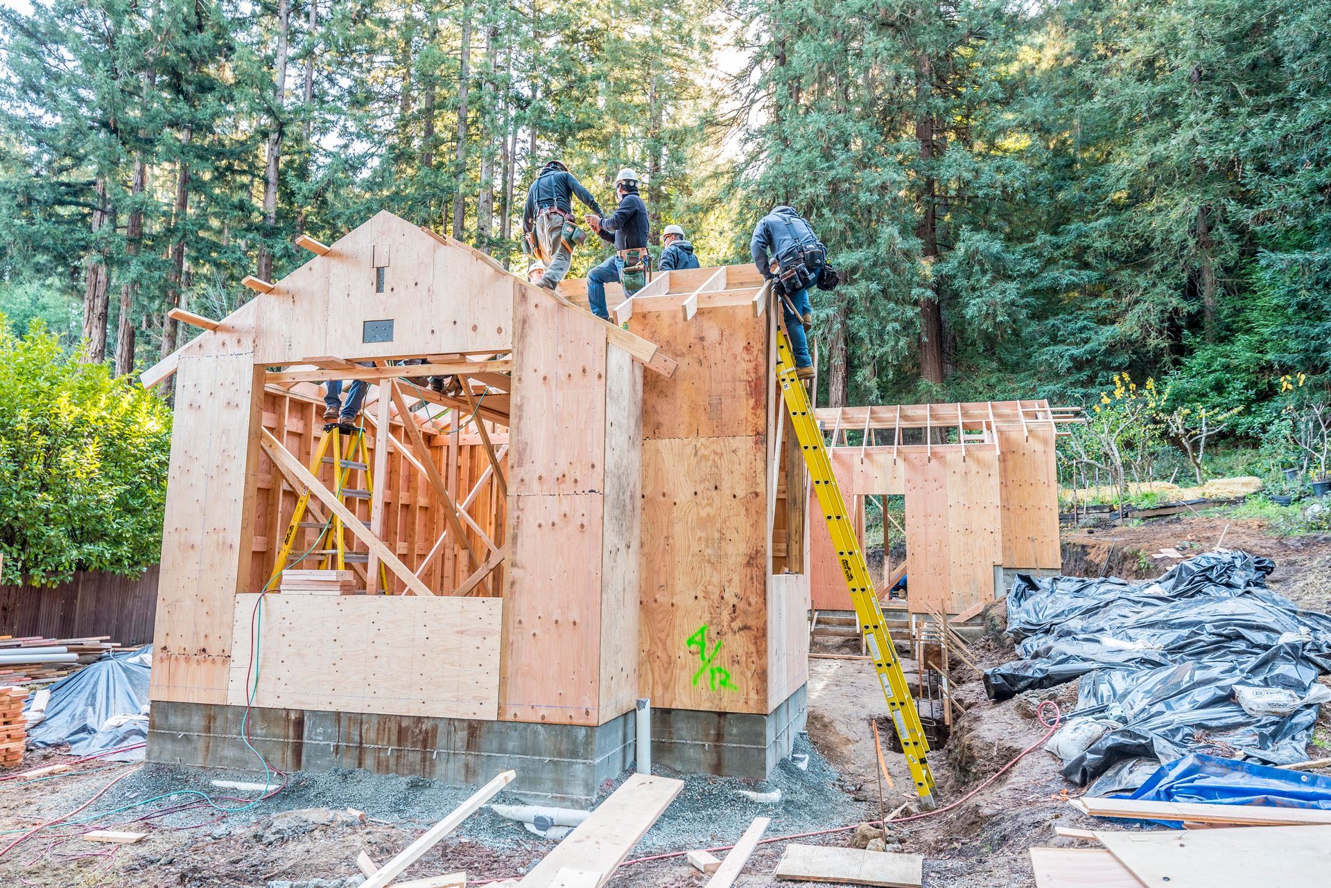 Wood-framed house under construction with workers on the roof in a wooded area