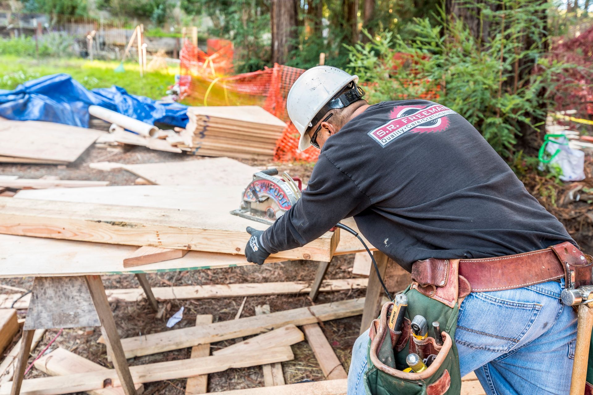 Worker in hard hat cutting wood at a construction site with lumber and debris nearby