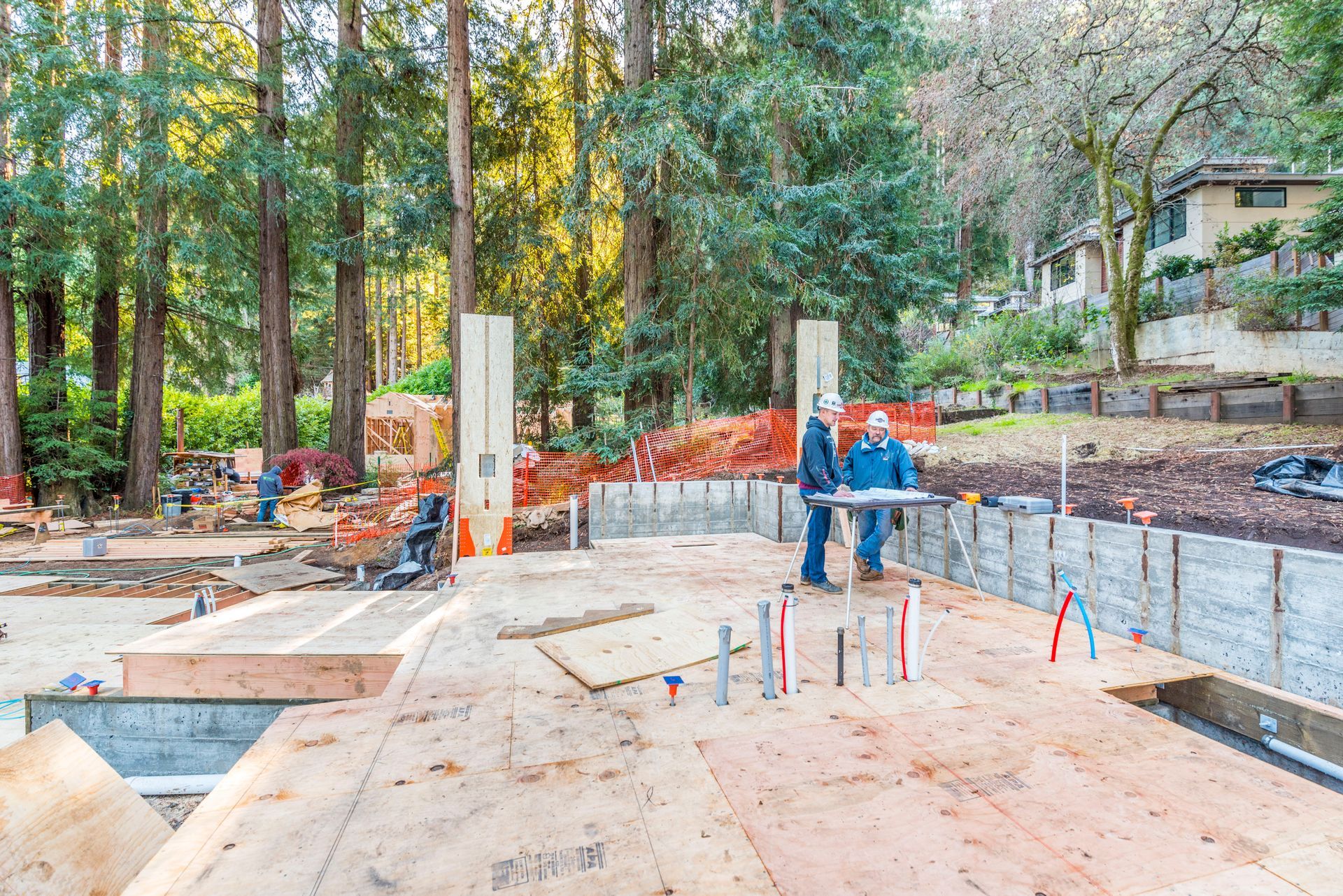 Construction site with workers pouring concrete foundation in a wooded residential area