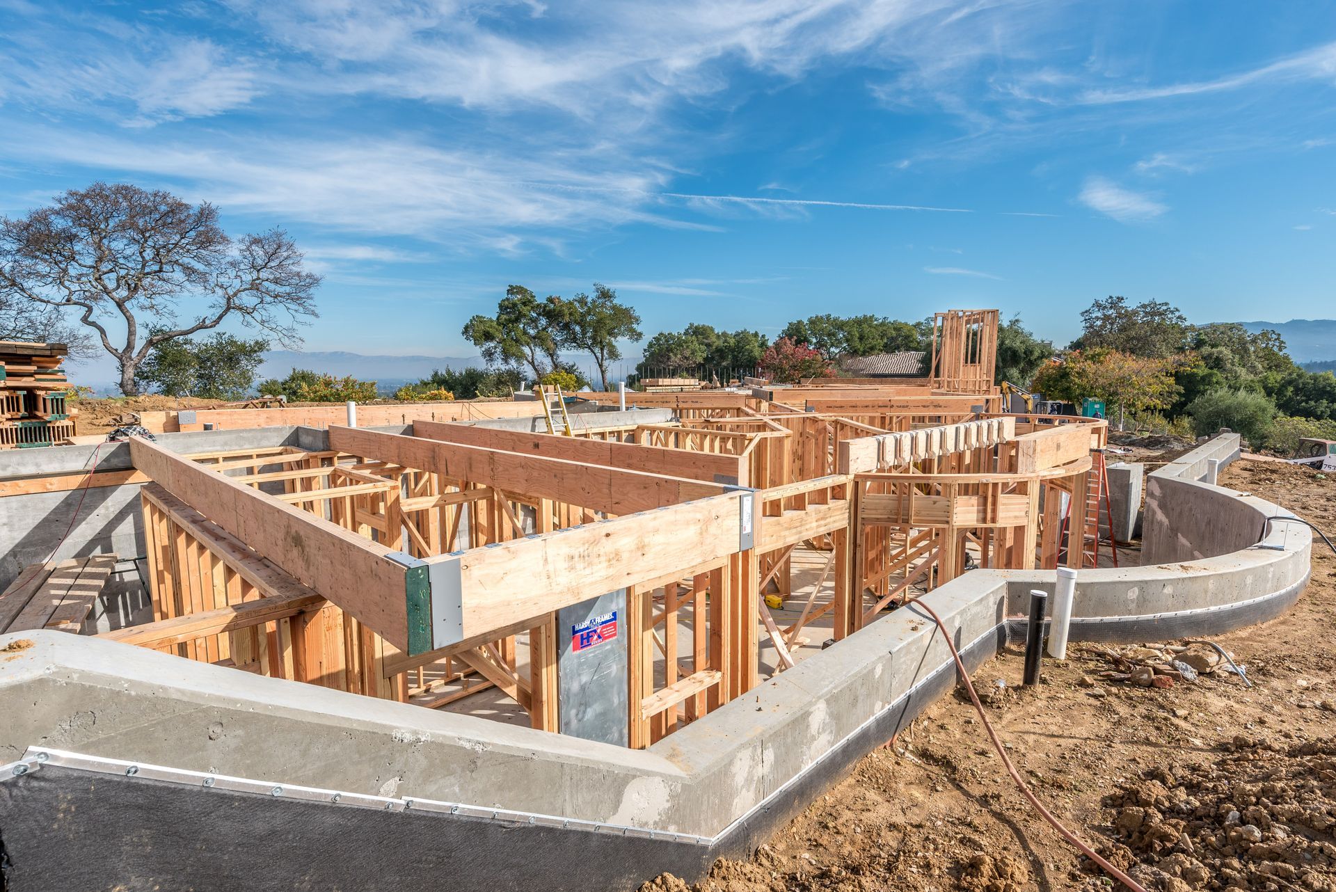 Partially built wooden house foundation with concrete walls on a dry hillside under a blue sky