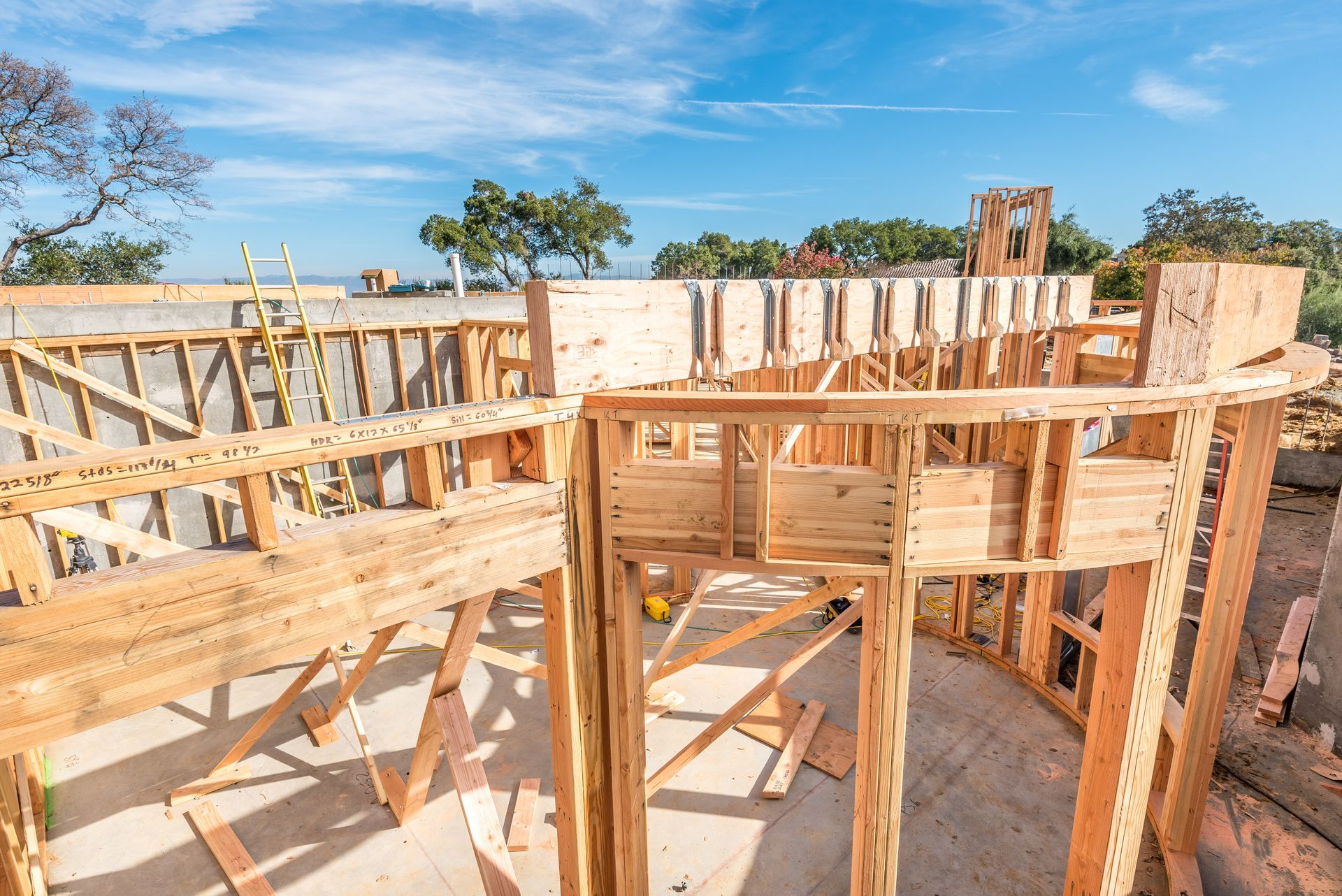 Wooden house frame under construction with exposed beams against a blue sky.
