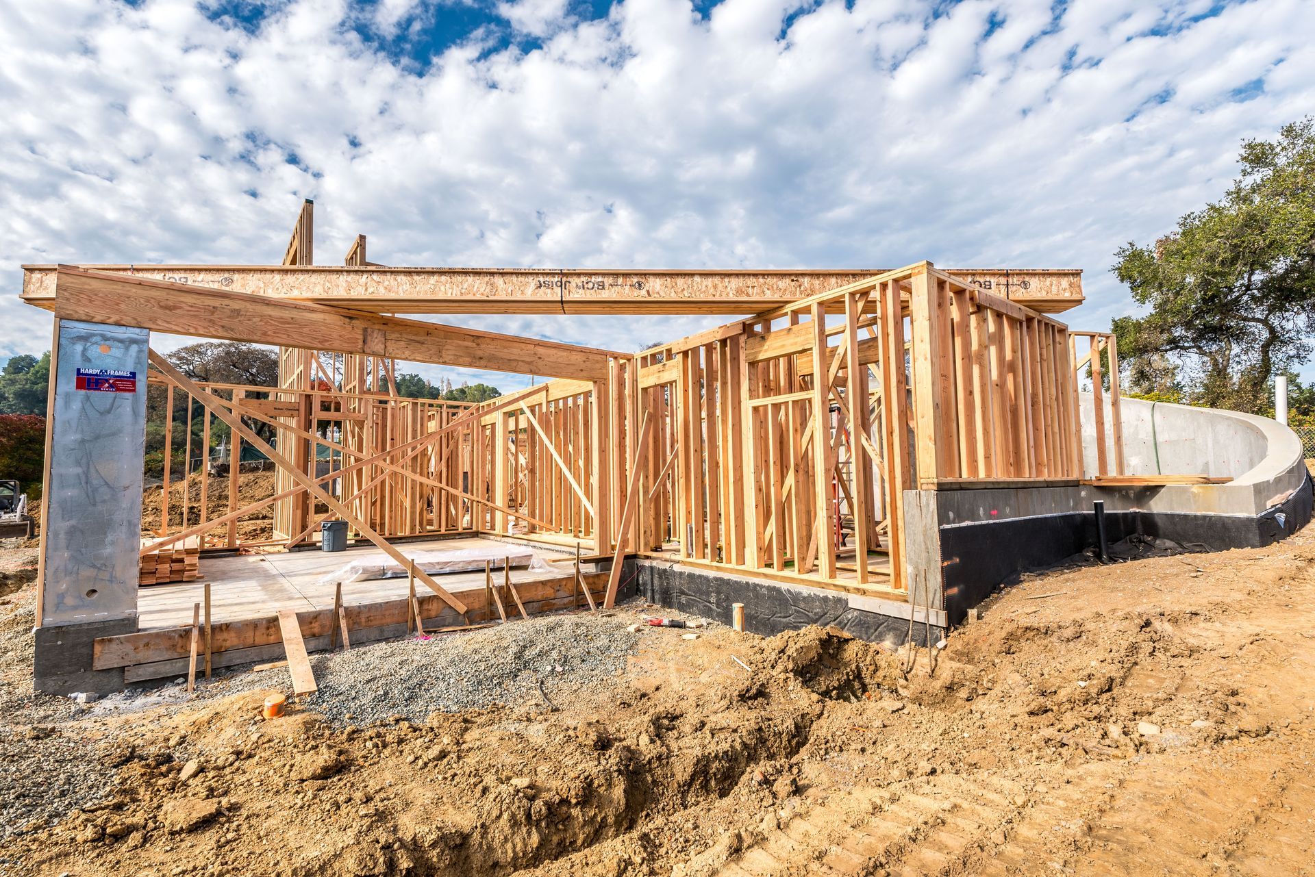 Wood-framed house under construction on a dirt lot under a blue sky