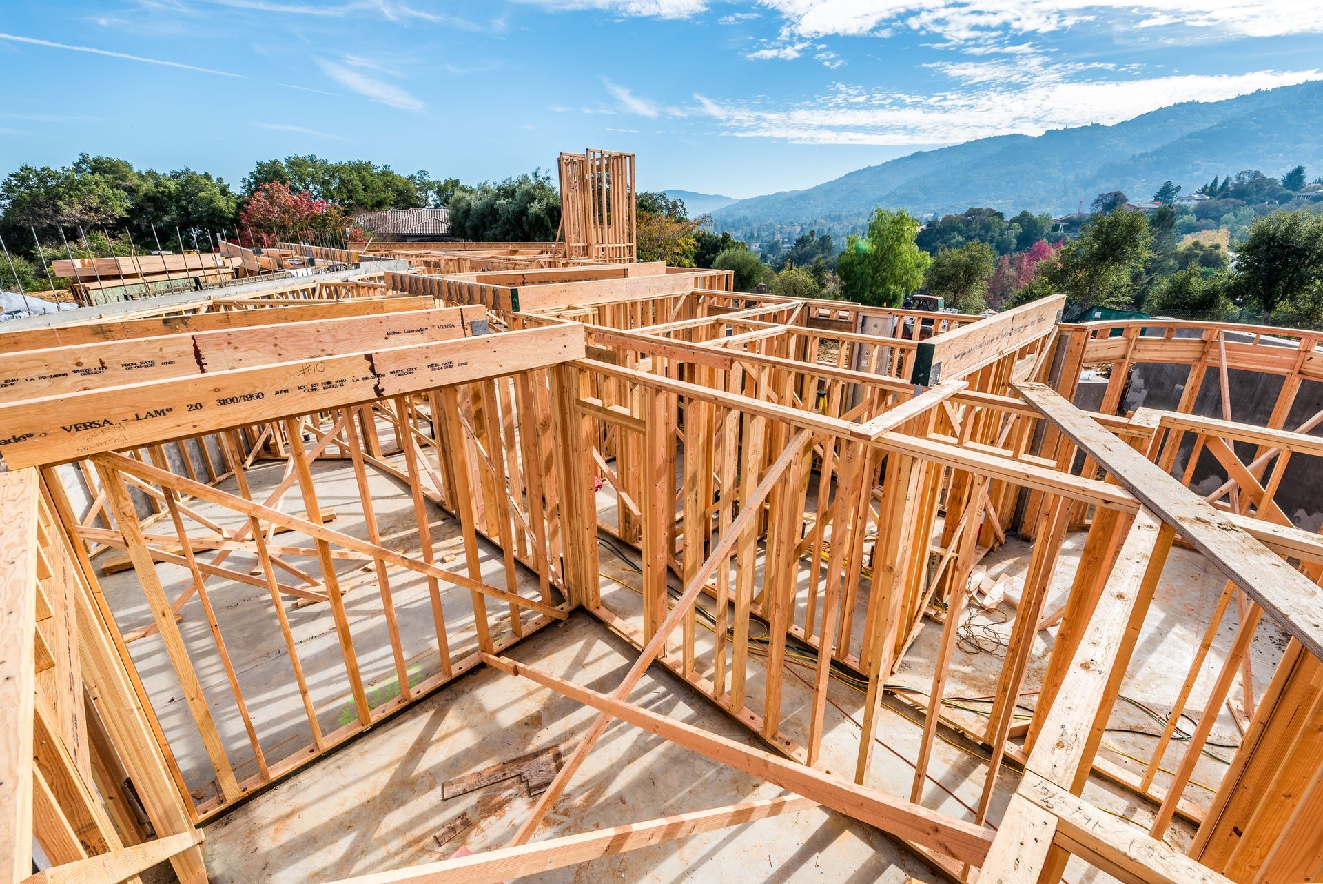 Wood-framed house under construction with open framing, mountain view, and blue sky in the background