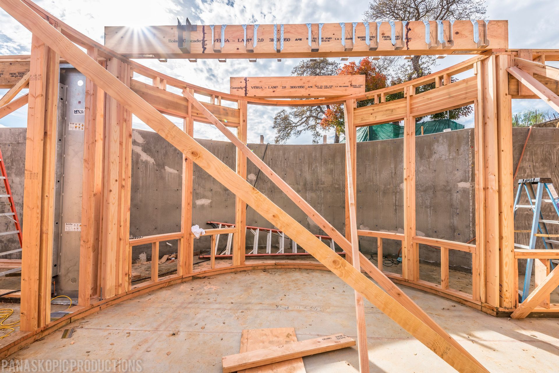 Wooden house framing under construction with diagonal braces and a concrete floor visible.