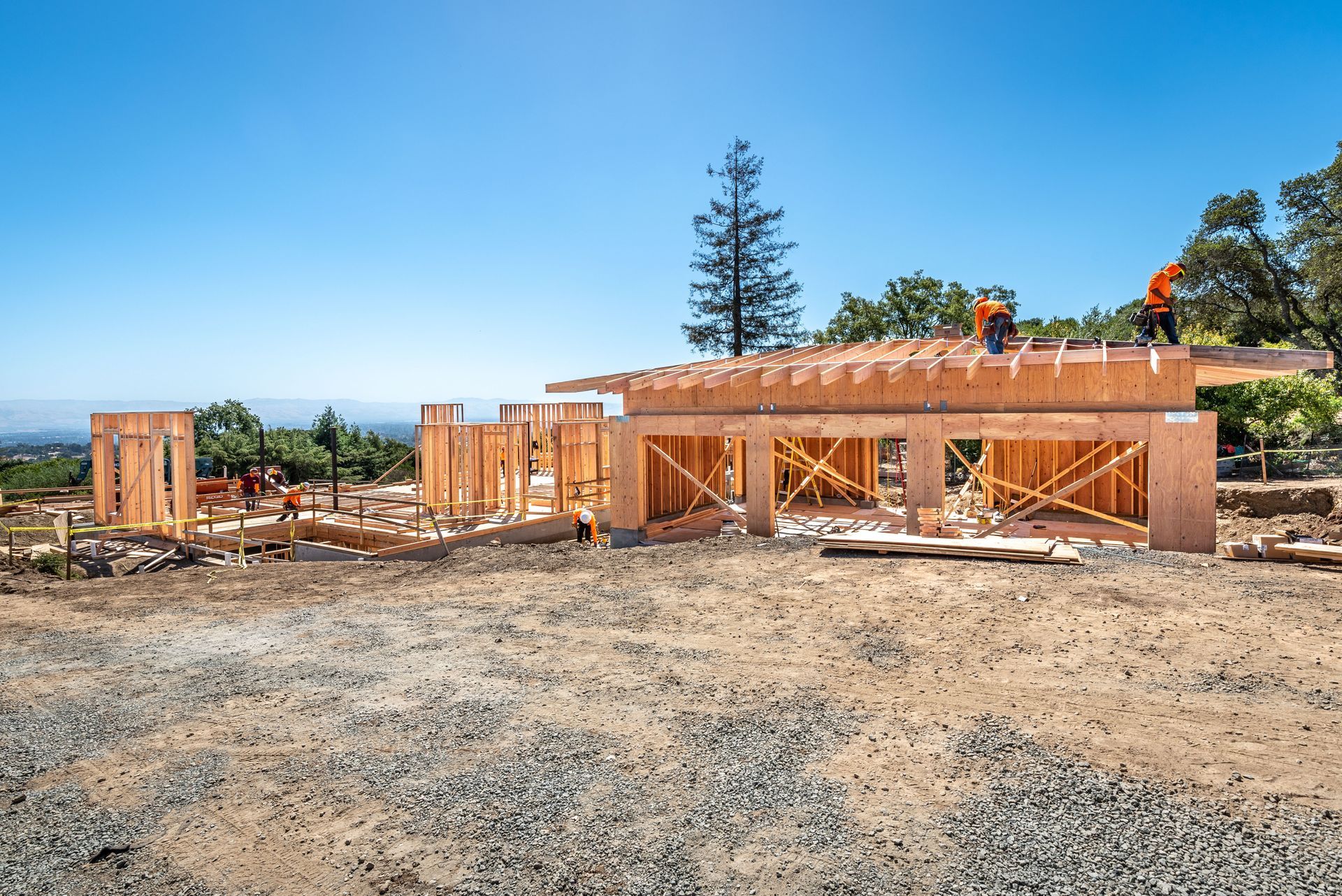 Partially built house framing on a gravel lot under a clear blue sky
