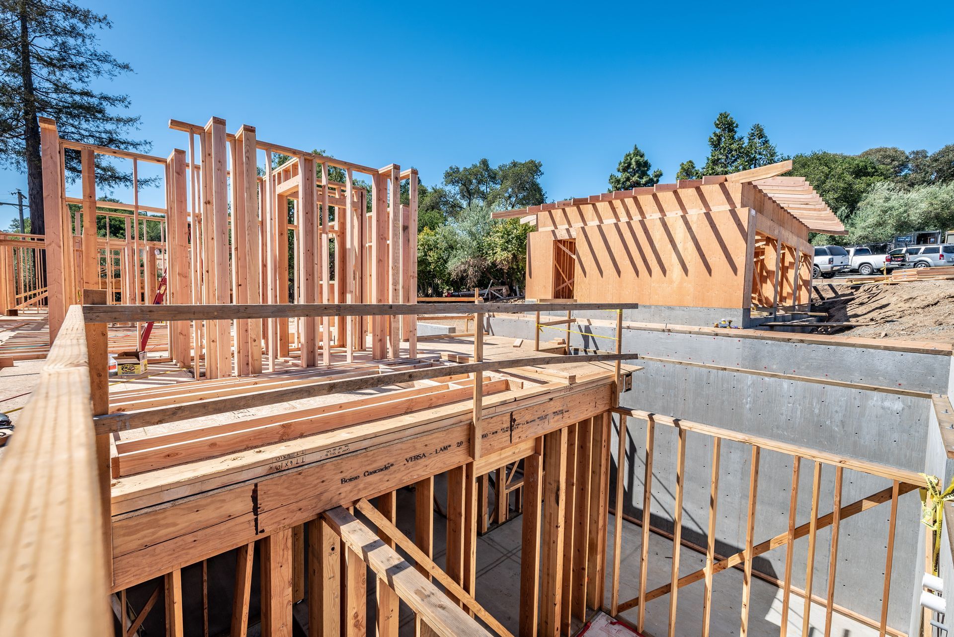 Wood-framed house under construction with exposed beams and concrete foundation under a clear blue sky