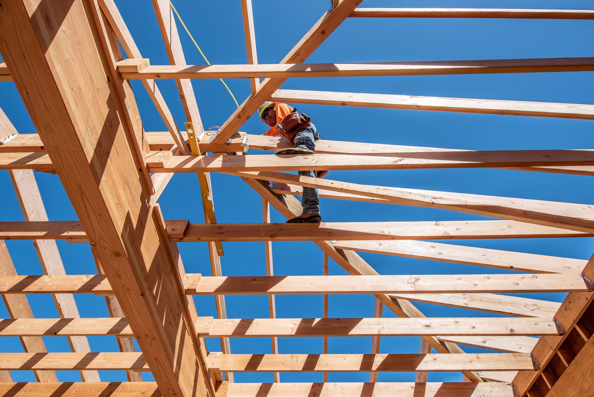 Construction worker on wooden roof framing against a bright blue sky