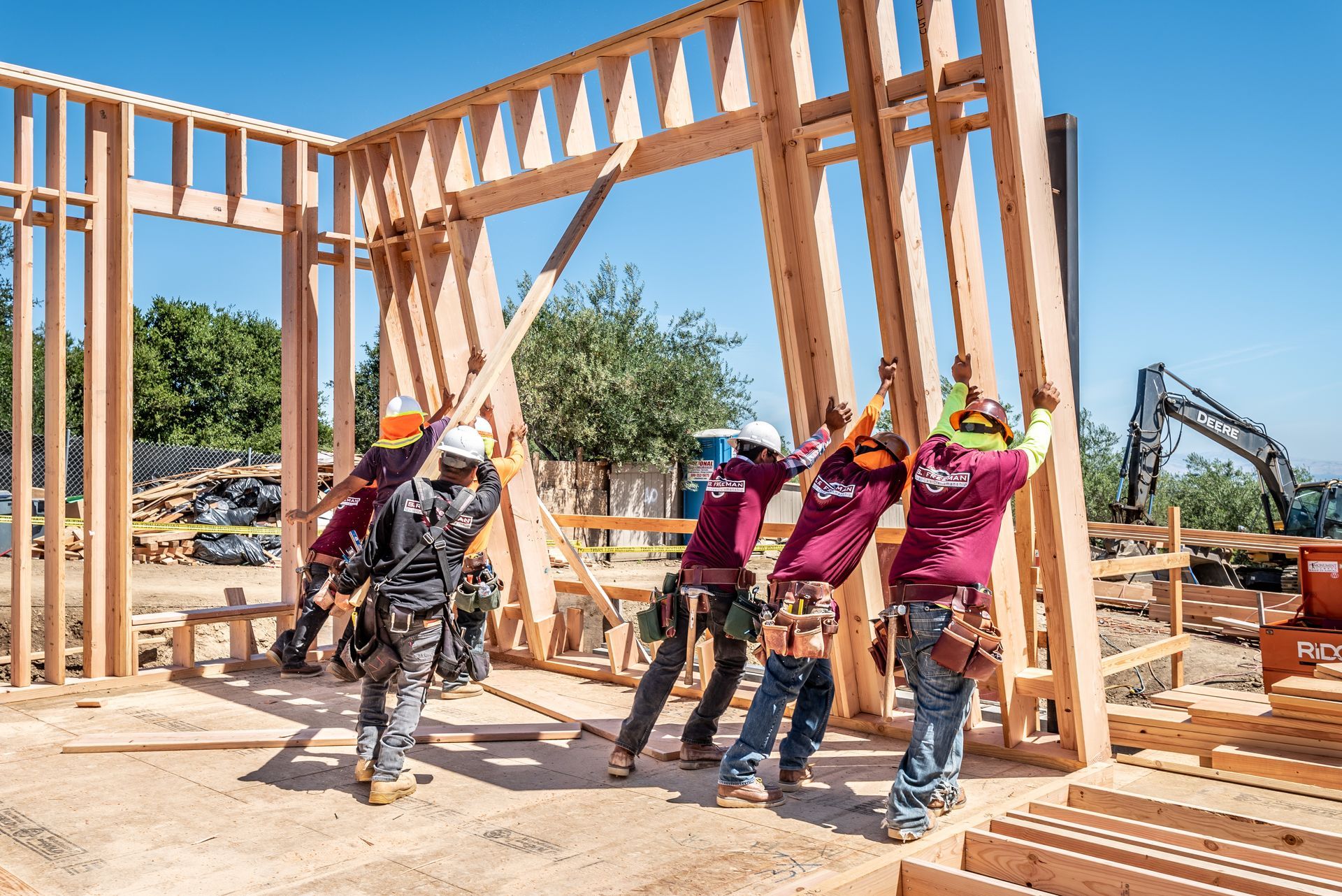 Workers raising a wooden house frame at a construction site on a sunny day