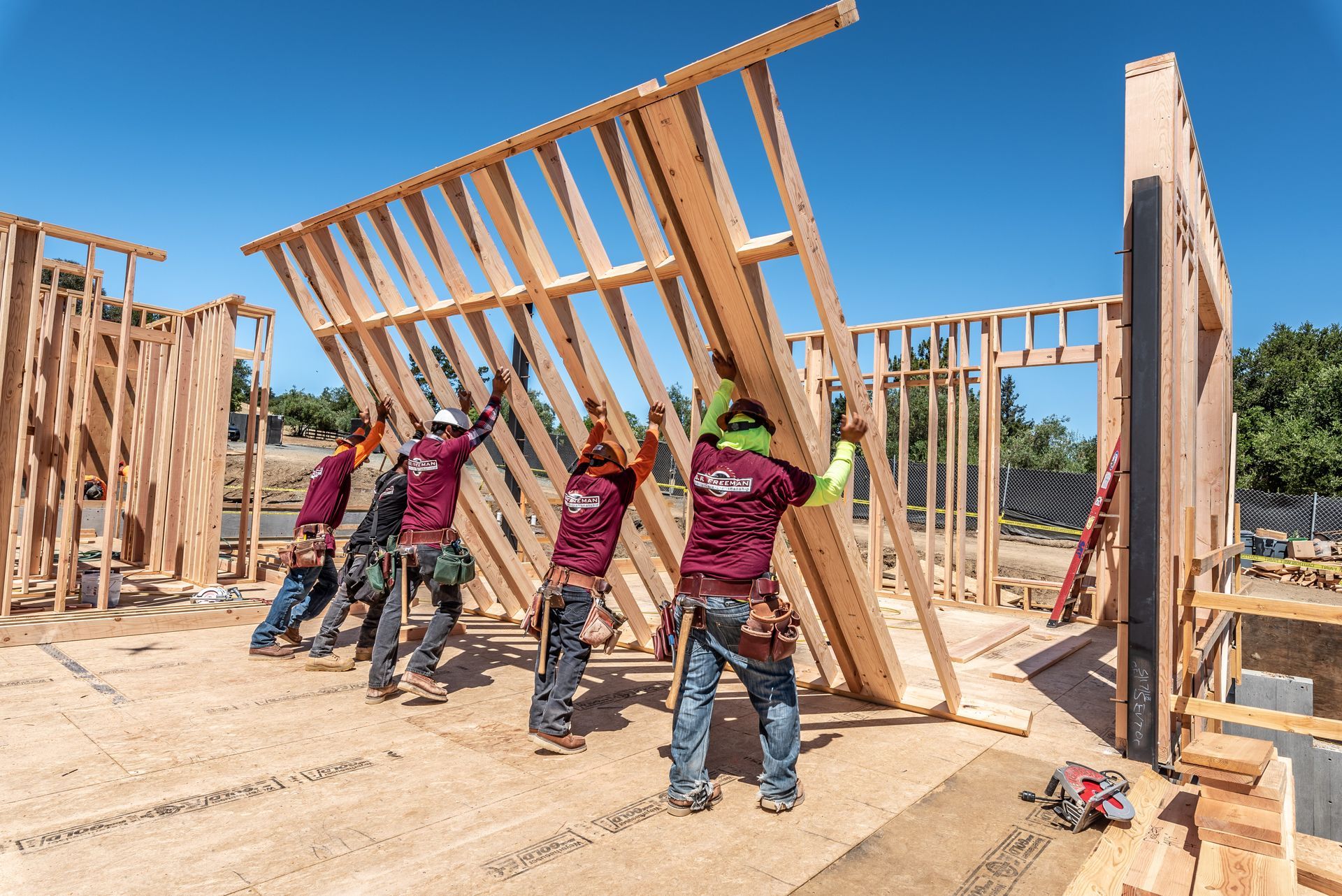 Workers raising a wooden wall frame on a sunny construction site
