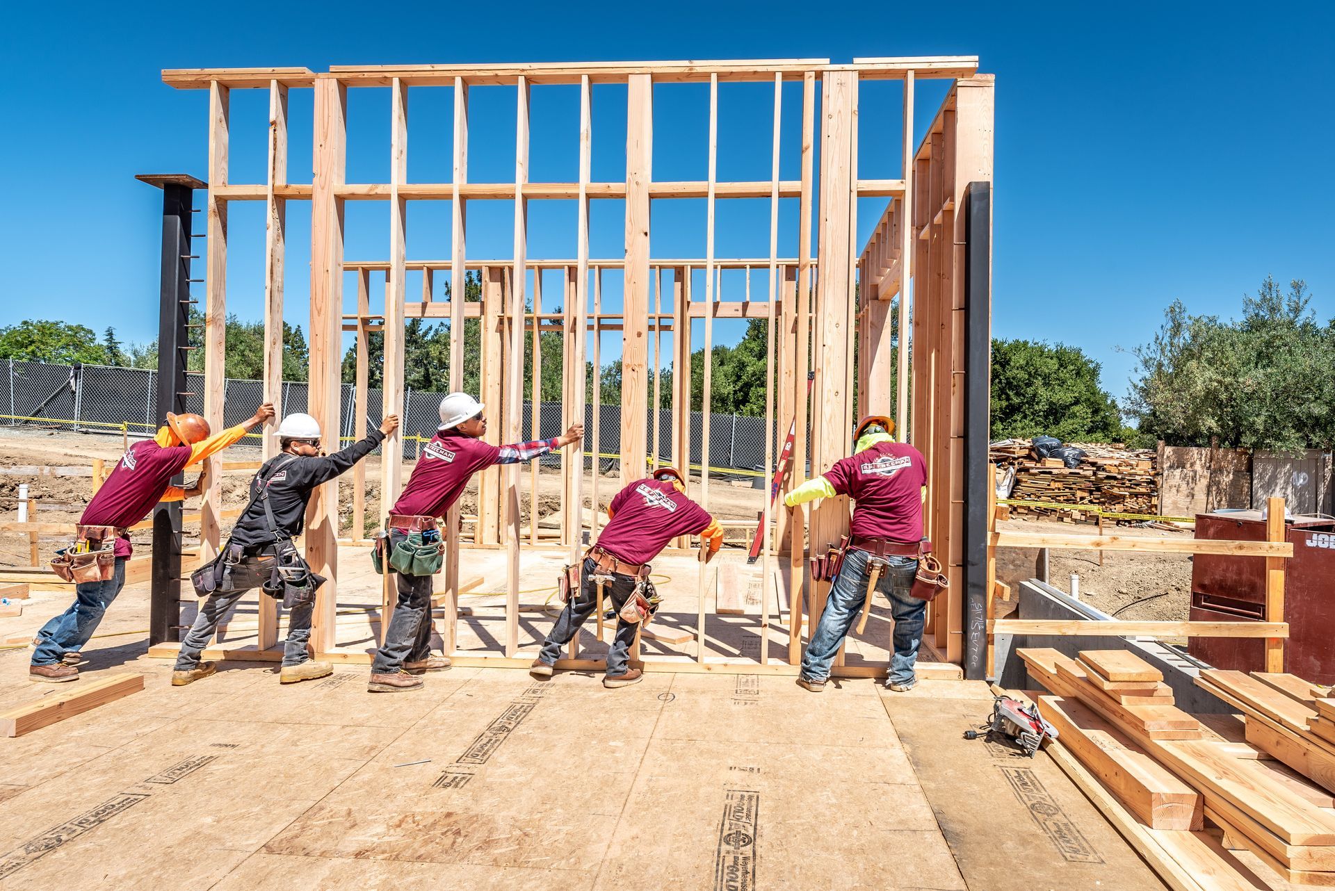 Construction workers framing a house with wooden beams on a sunny job site