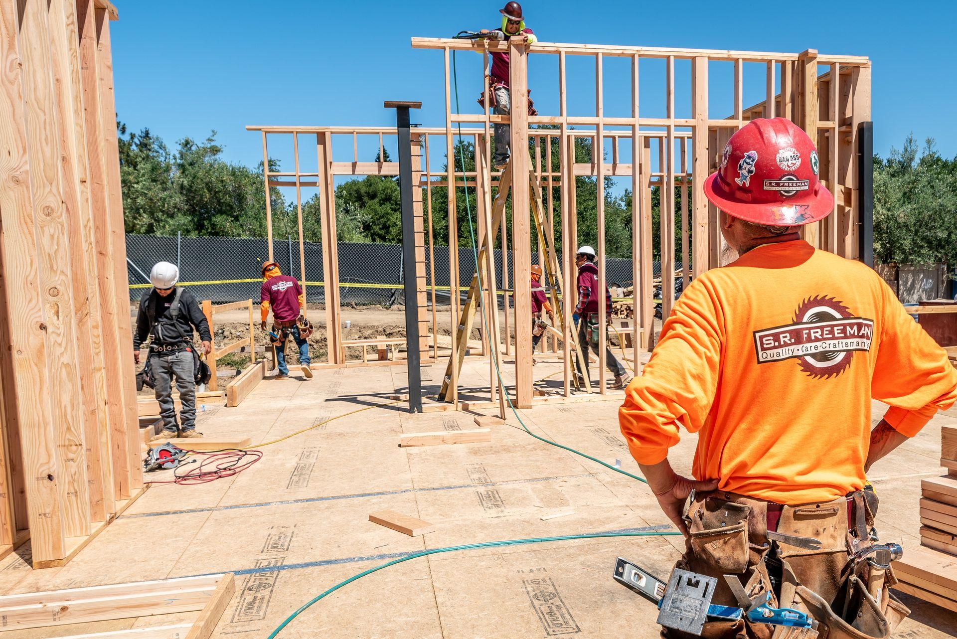 Construction workers framing a house, with a worker in an orange safety shirt in the foreground