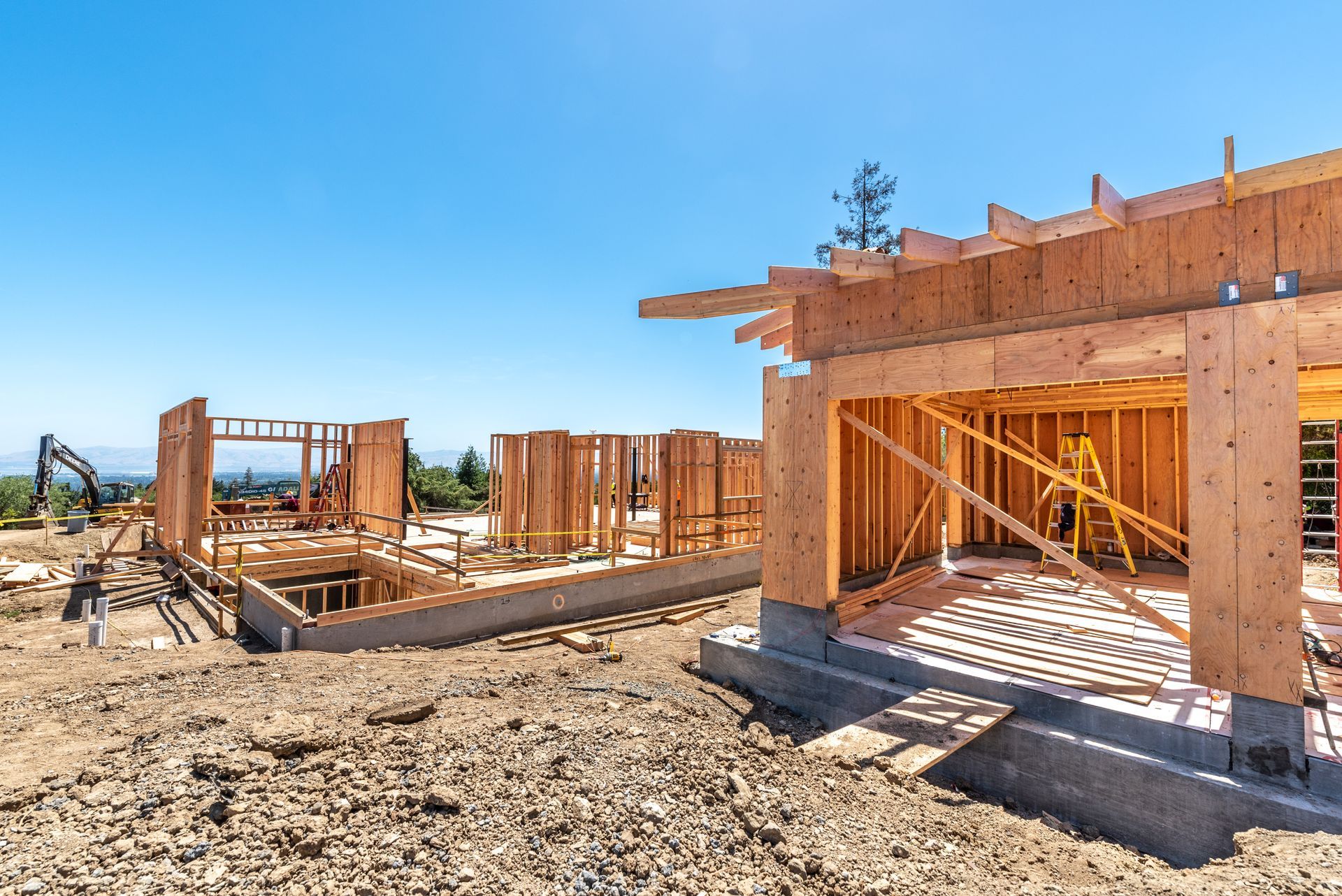 Partially built wooden house framing on a sunny construction site under a blue sky