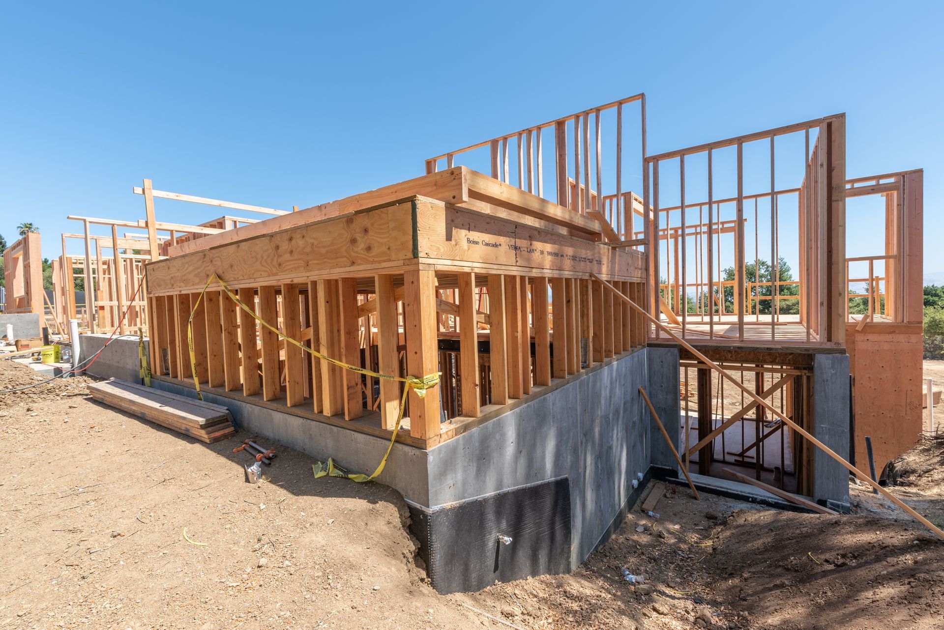 Wood-framed house under construction with concrete foundation and exposed framing on a sunny day