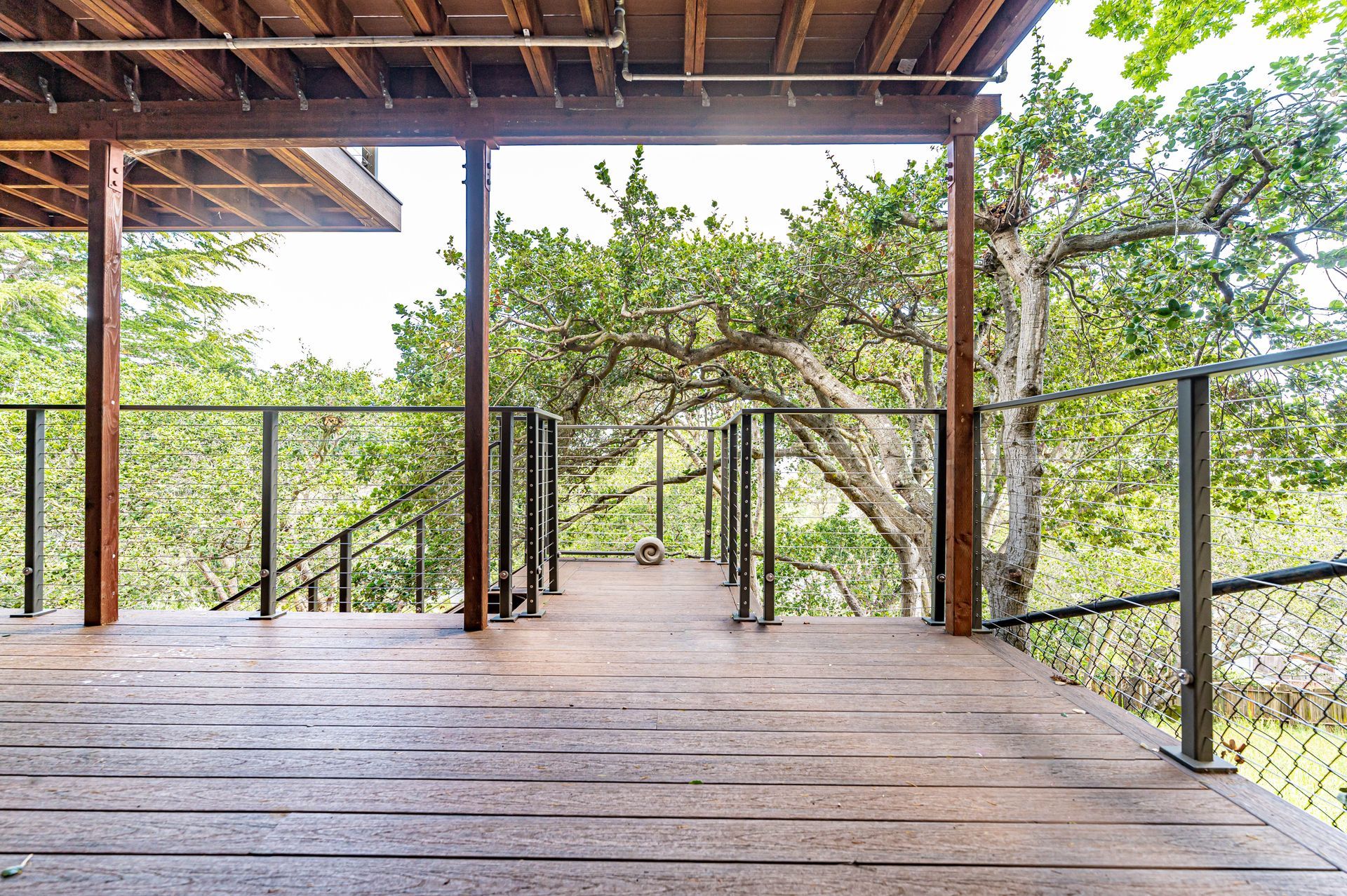 Wooden deck with railings under a roof, overlooking green trees and a hillside.