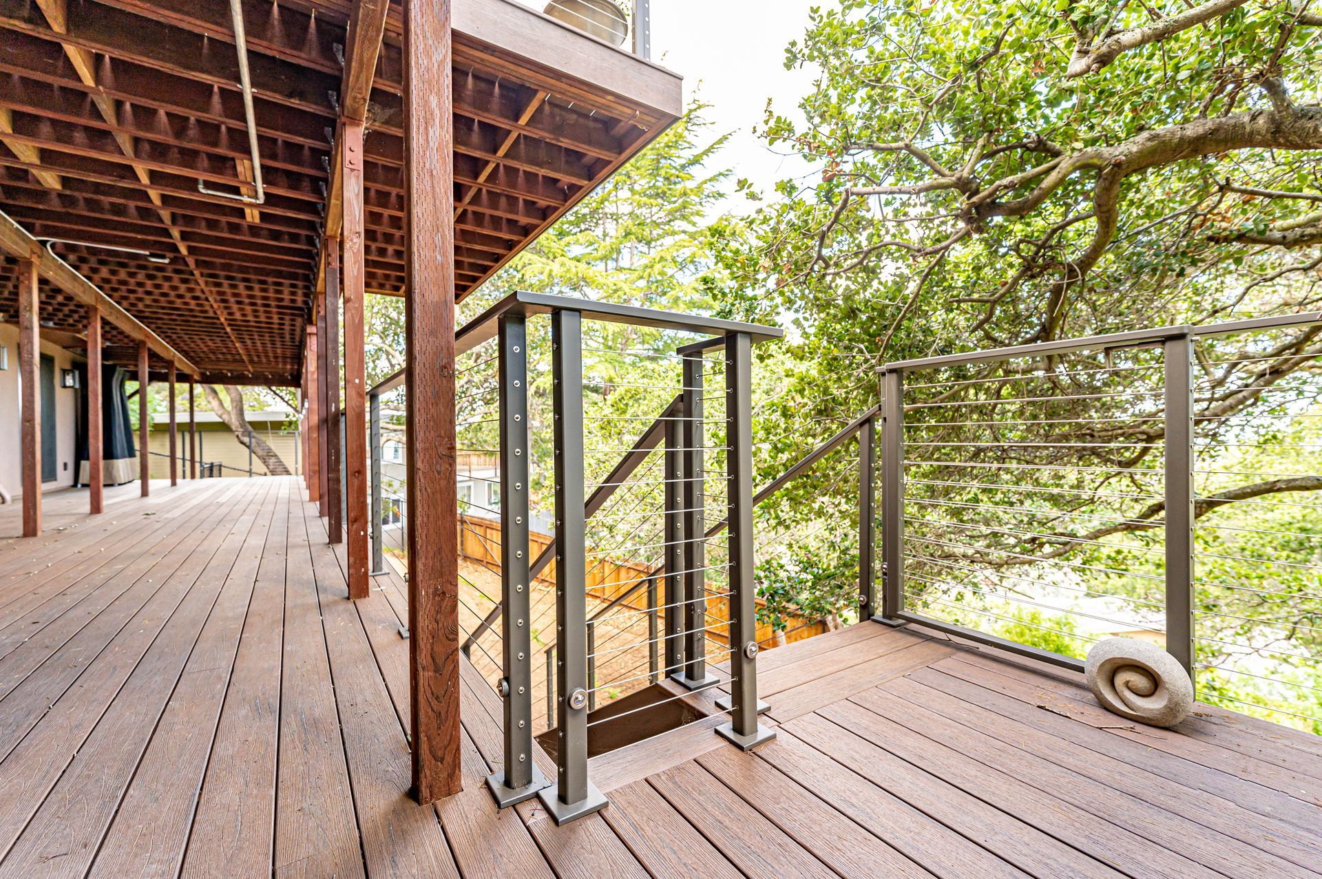 Wooden deck with stairs and metal railings overlooking a leafy hillside