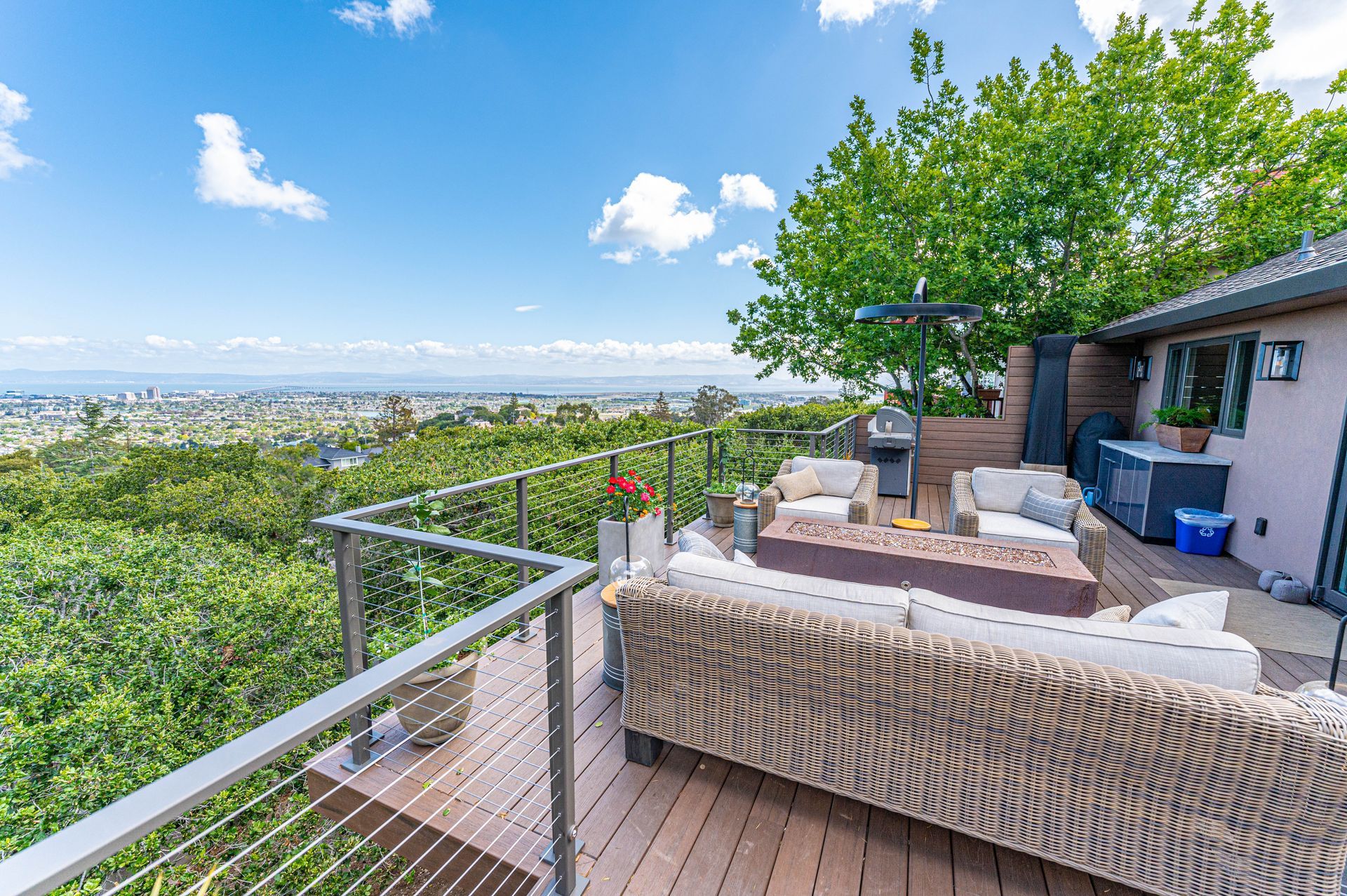Patio with wicker furniture and glass railing overlooking a city skyline and blue sky