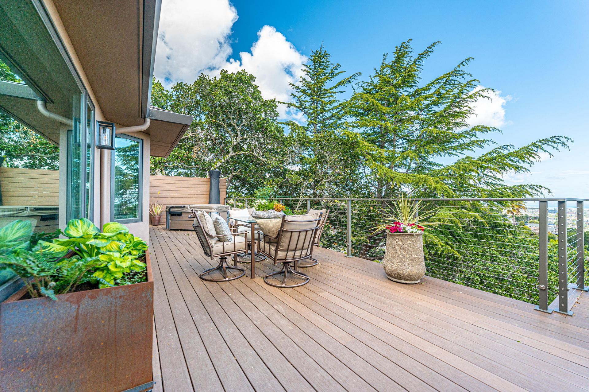 Outdoor deck with dining table, chairs, potted plants, and a view of trees and sky