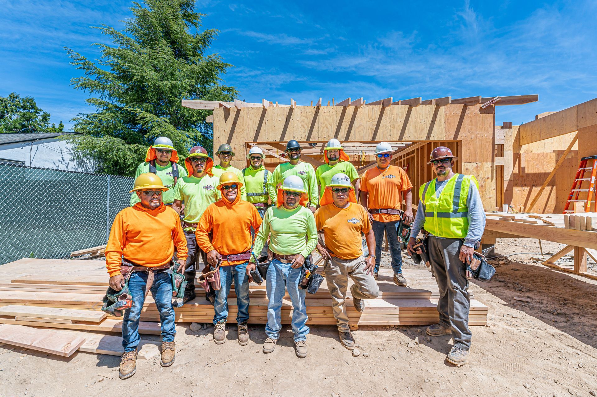 Construction crew in orange and green safety gear posing at a wooden house frame site