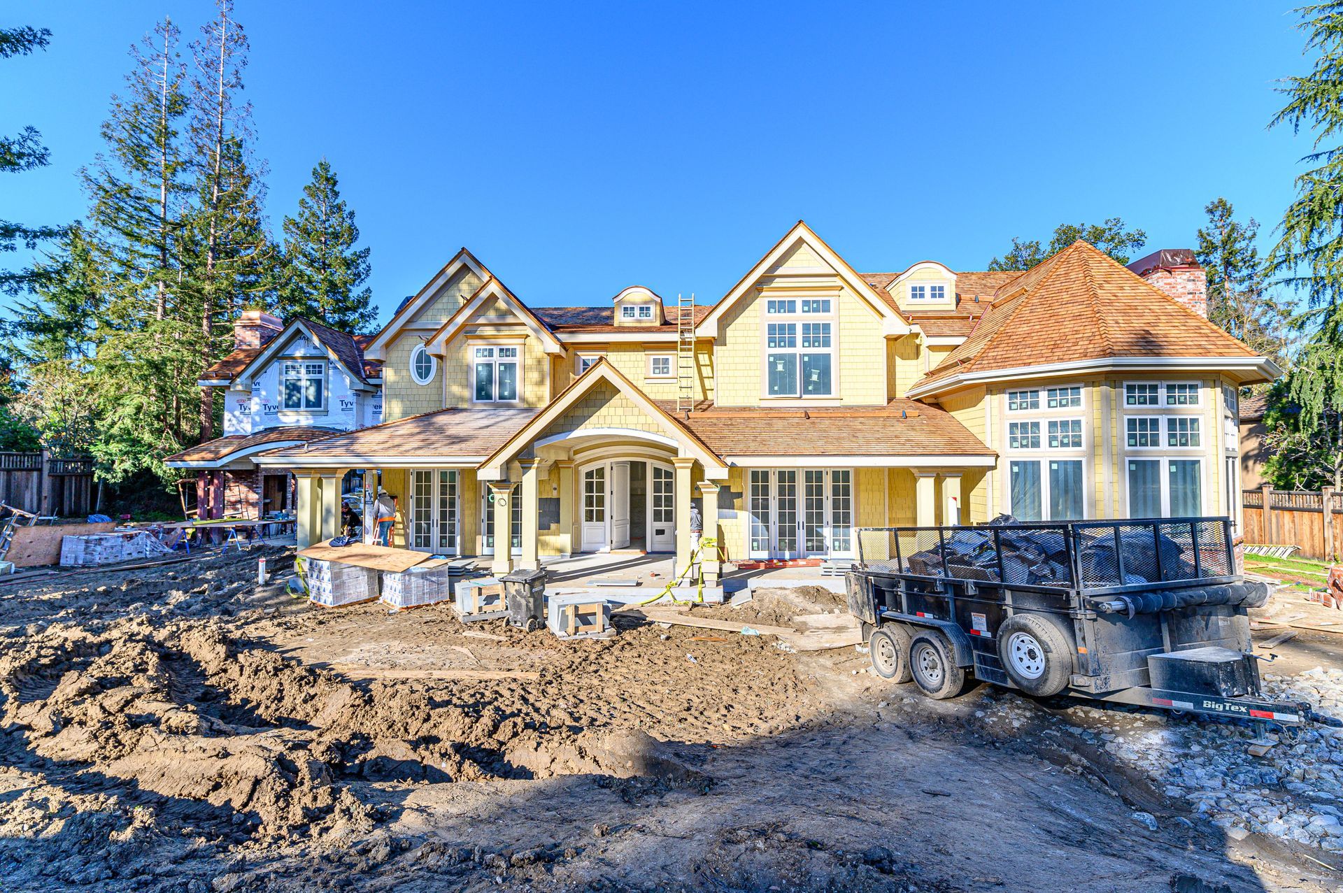Newly built suburban house with a muddy front yard and construction equipment under a bright blue sky