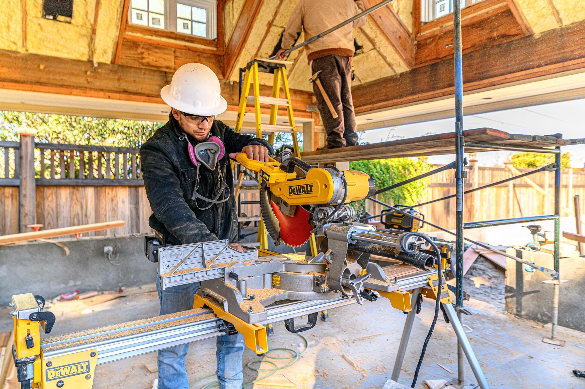Worker using a miter saw in a sunlit workshop under construction