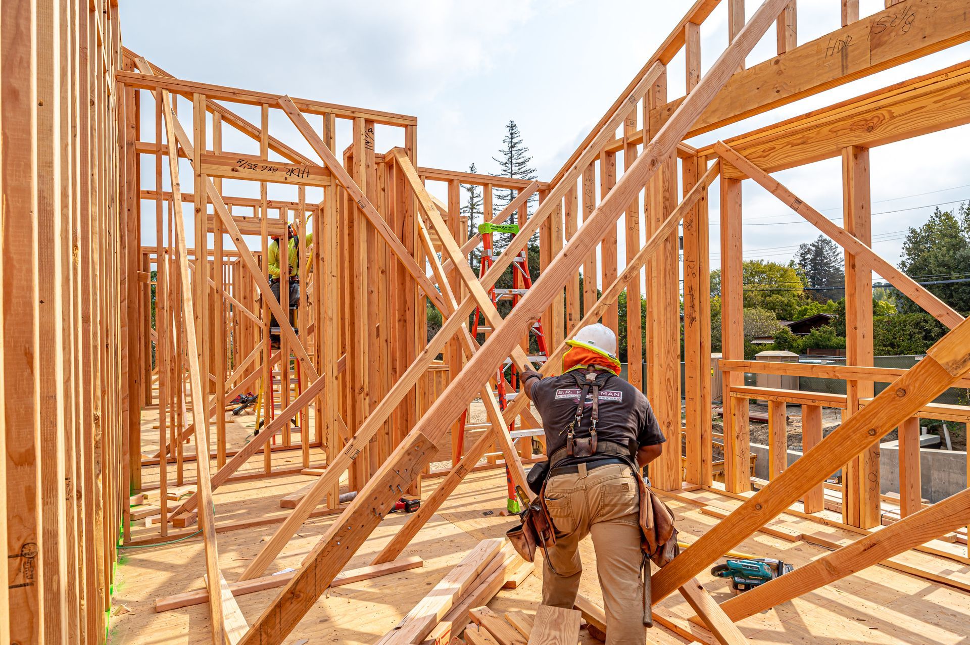 Construction workers framing a wooden house, with one worker carrying tools inside the structure.