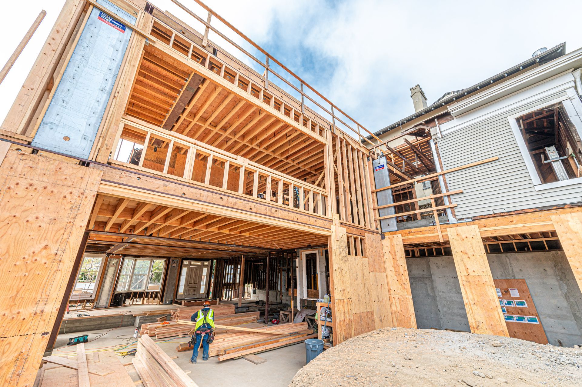 Wood-framed building under construction with exposed plywood, scaffolding, and a worker in a hard hat