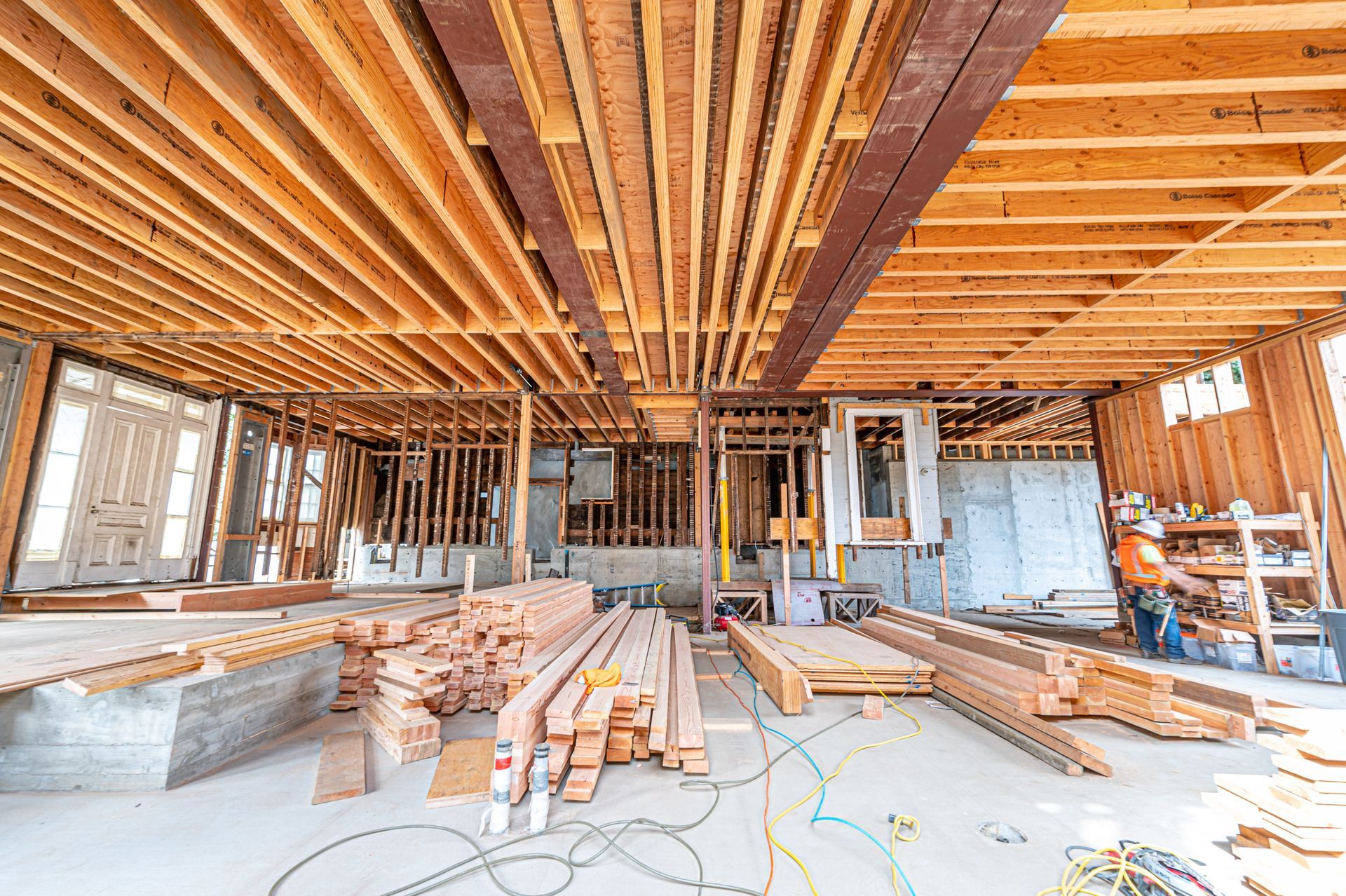 Construction site interior with exposed wooden ceiling beams, framing, and scattered lumber and tools