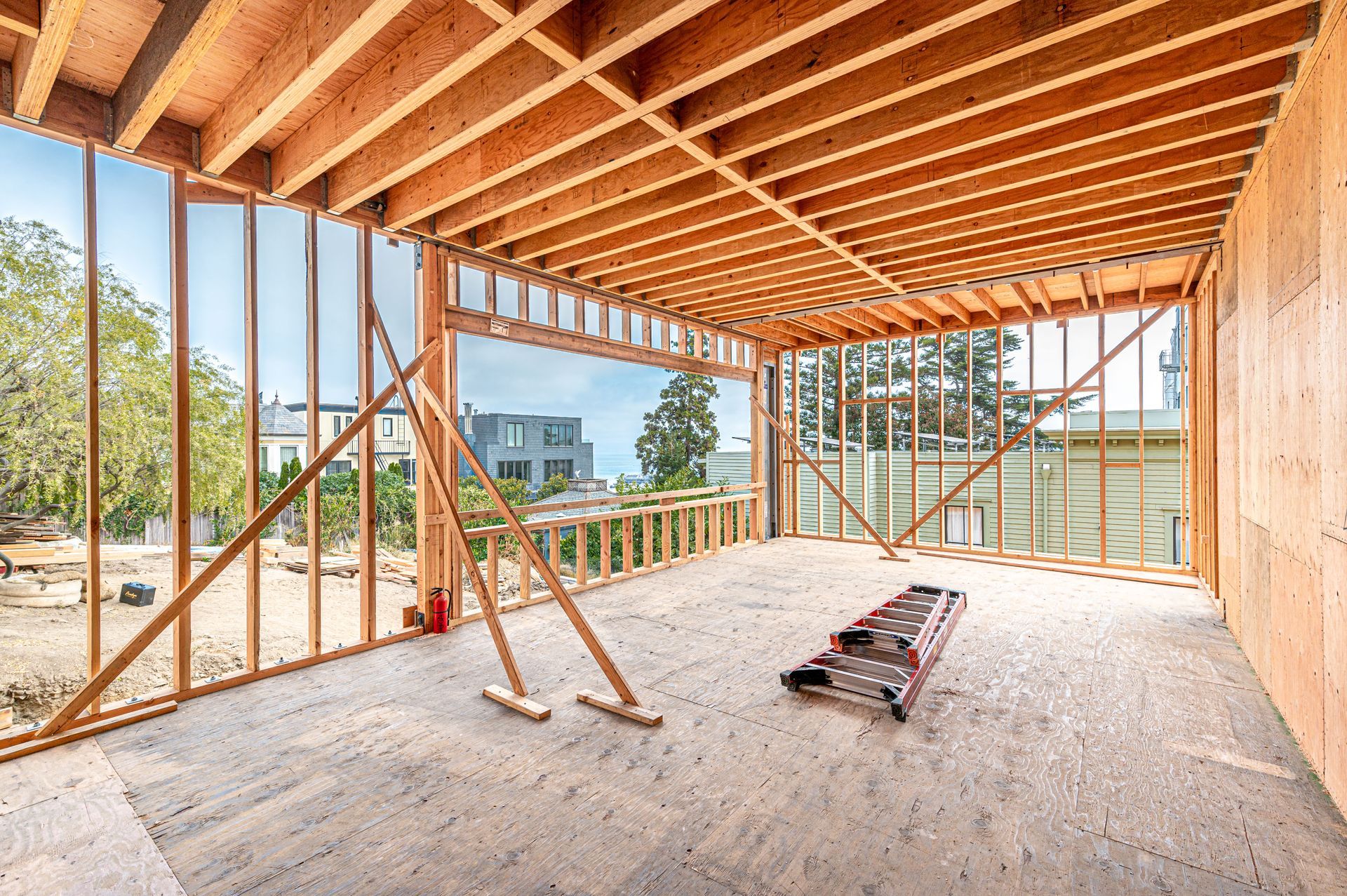 Unfinished room with exposed wooden beams, concrete floor, and large open window framing a city view.
