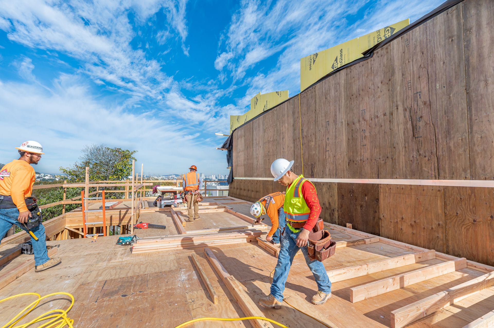 Construction workers on a site near a tall concrete wall under a bright blue sky