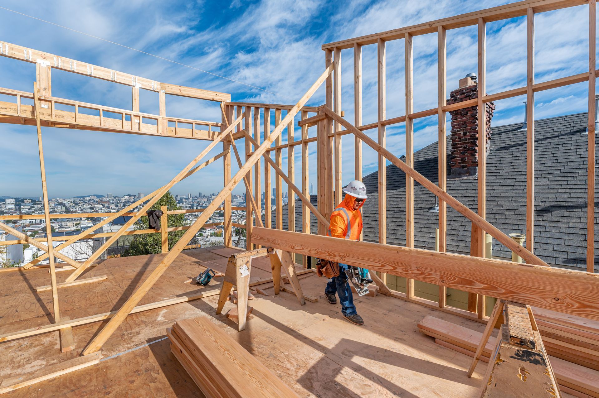 Construction worker on rooftop framing a house under a blue sky