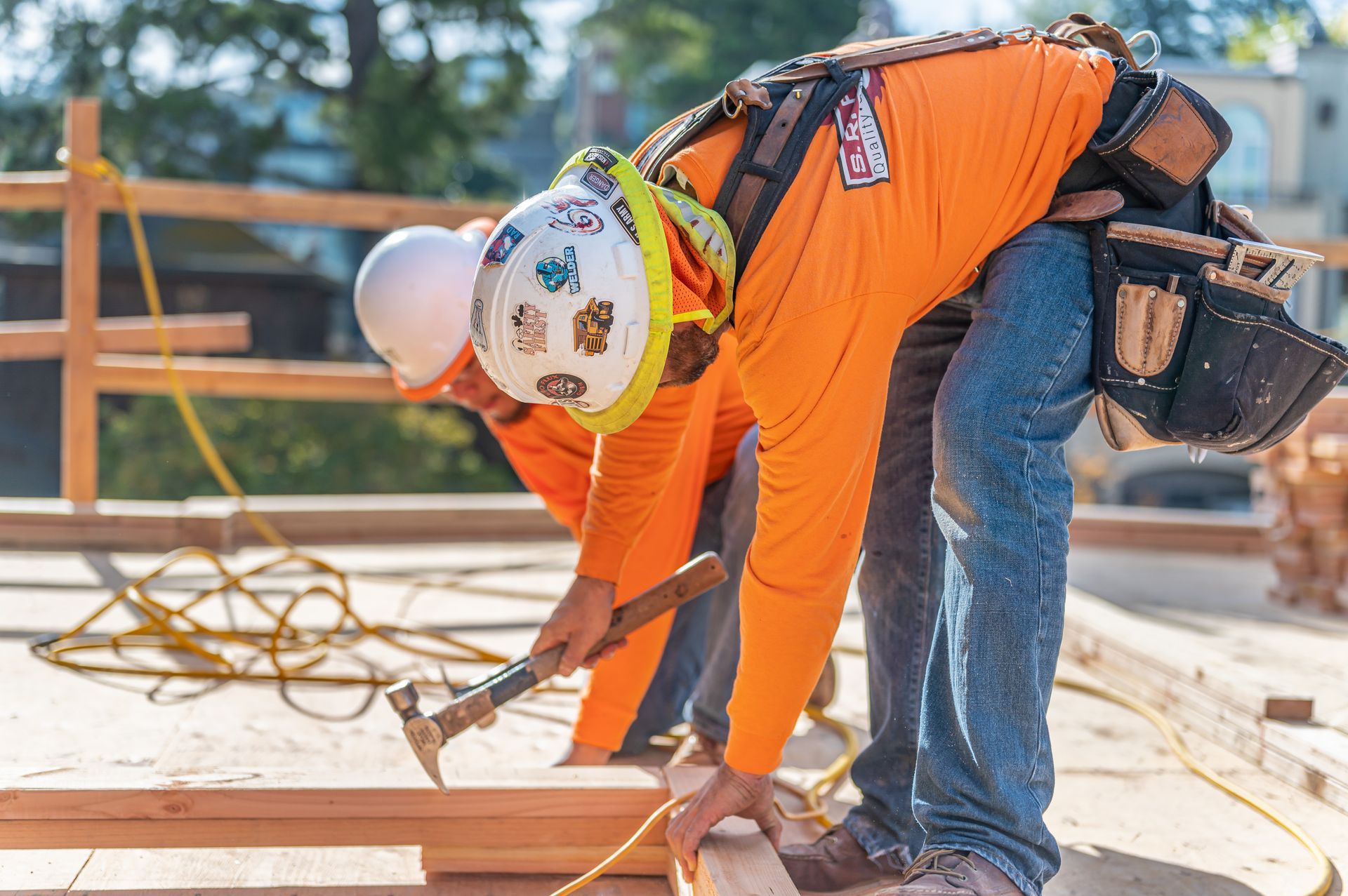 Construction worker in orange shirt and hard hat measuring wood at a building site