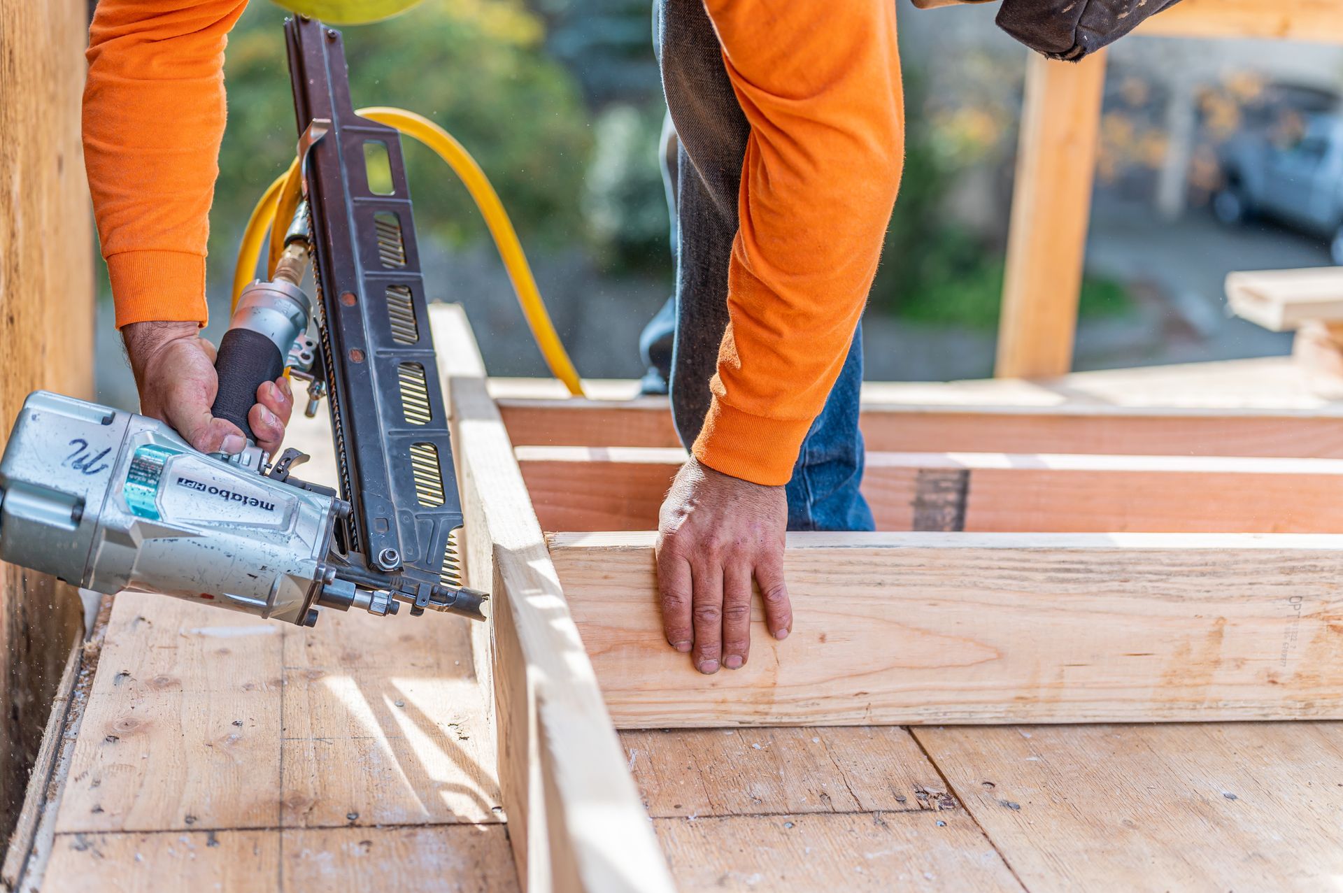 Worker using a nail gun to fasten wooden boards at a construction site