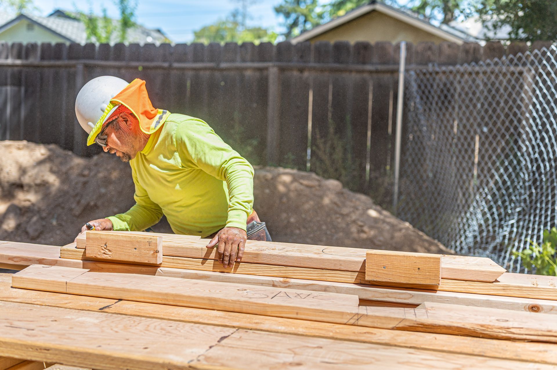 Worker in hard hat and safety vest measuring lumber at a construction site