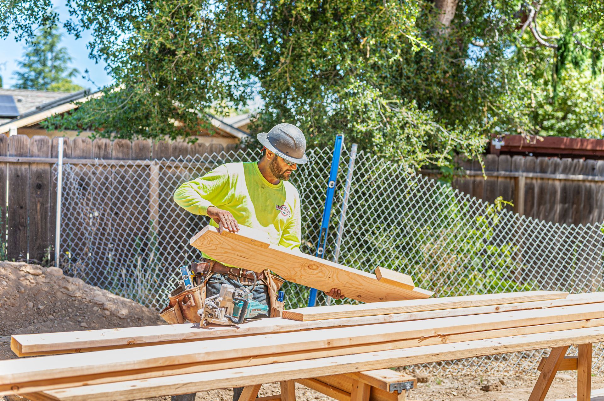 Worker in neon vest and hard hat cutting lumber on an outdoor sawhorse table