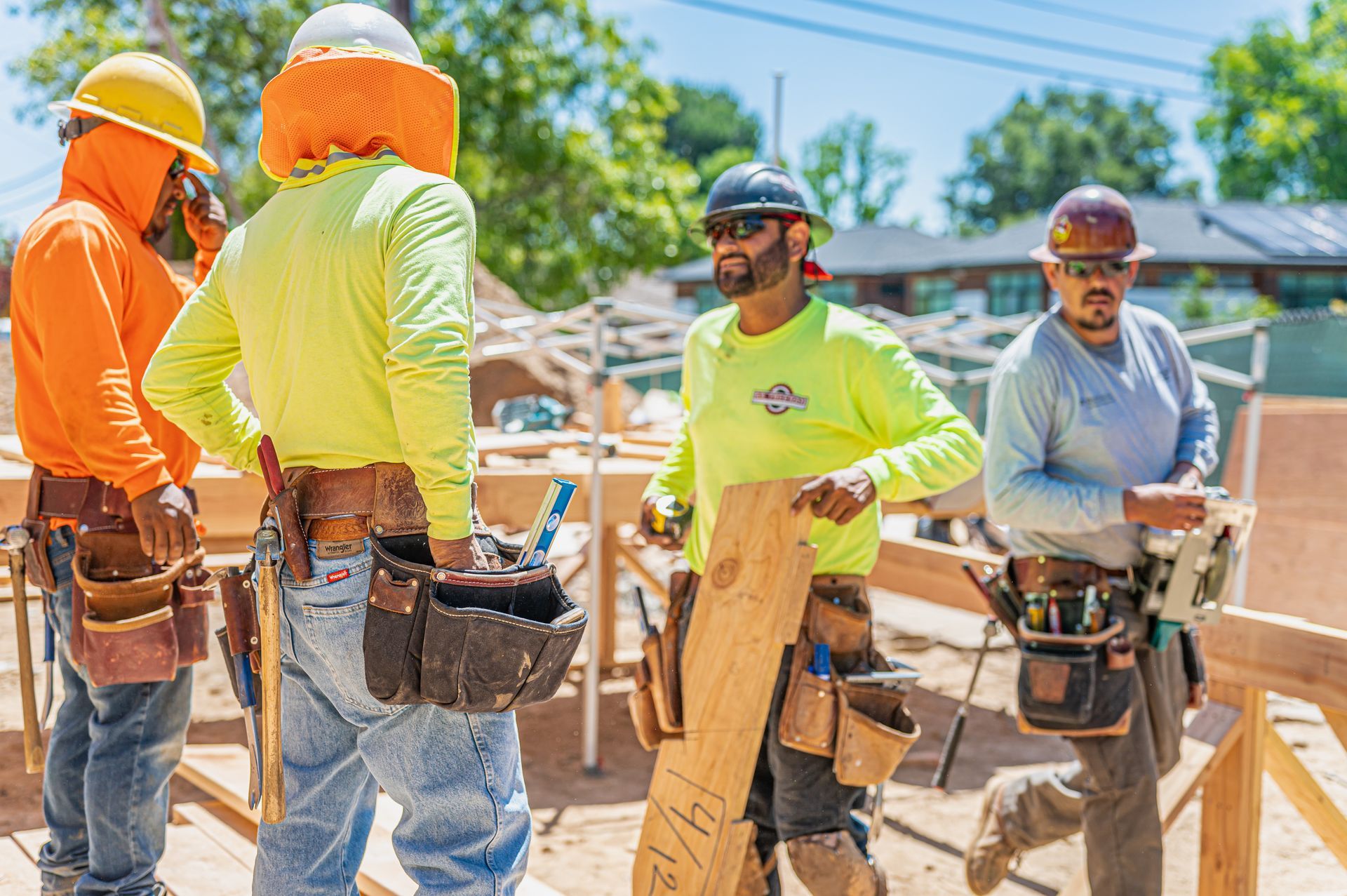 Construction workers in hard hats and safety gear stand on a building site holding tools.