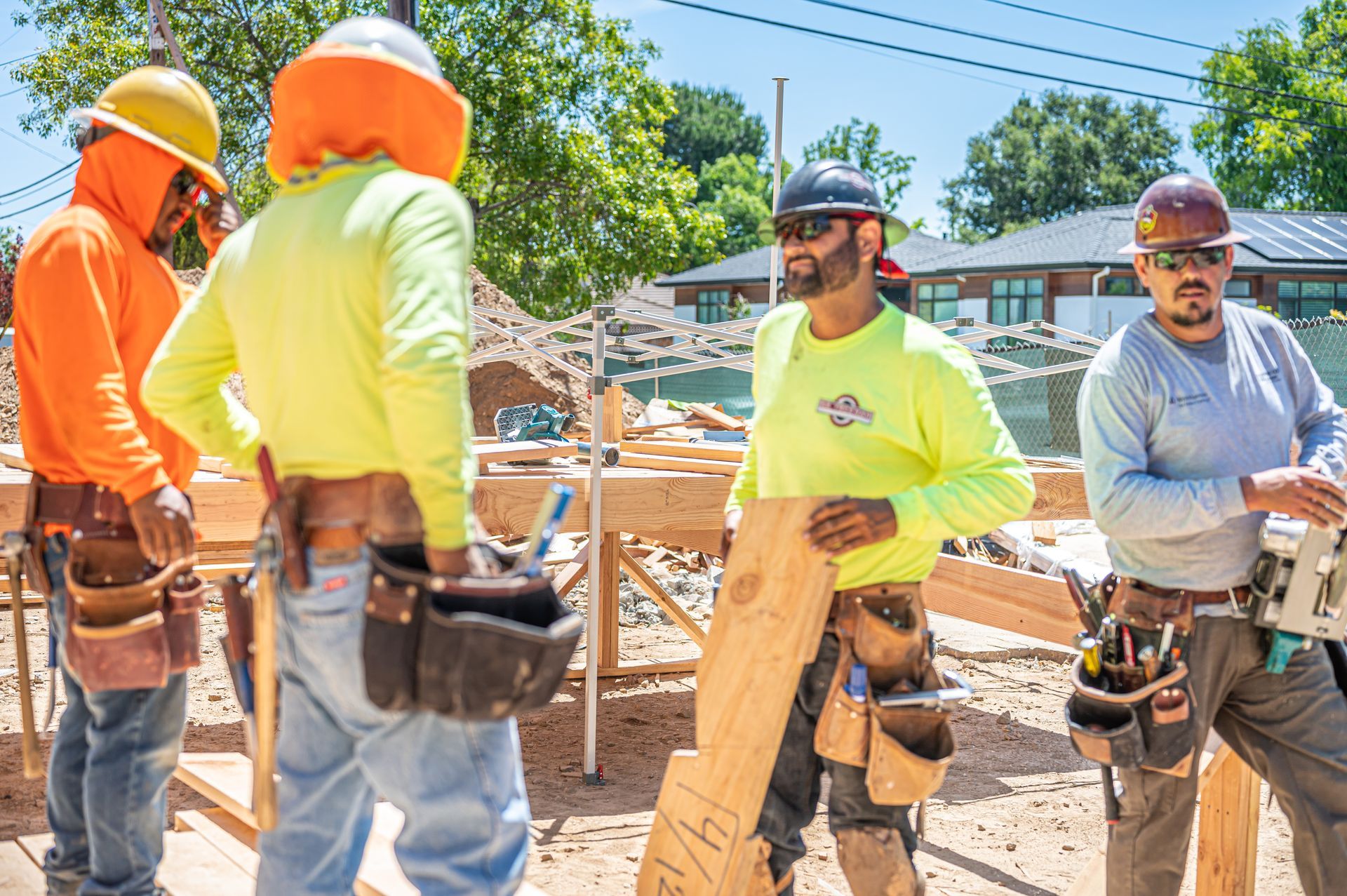 Construction workers in bright safety gear standing at a building site with tools and lumber.
